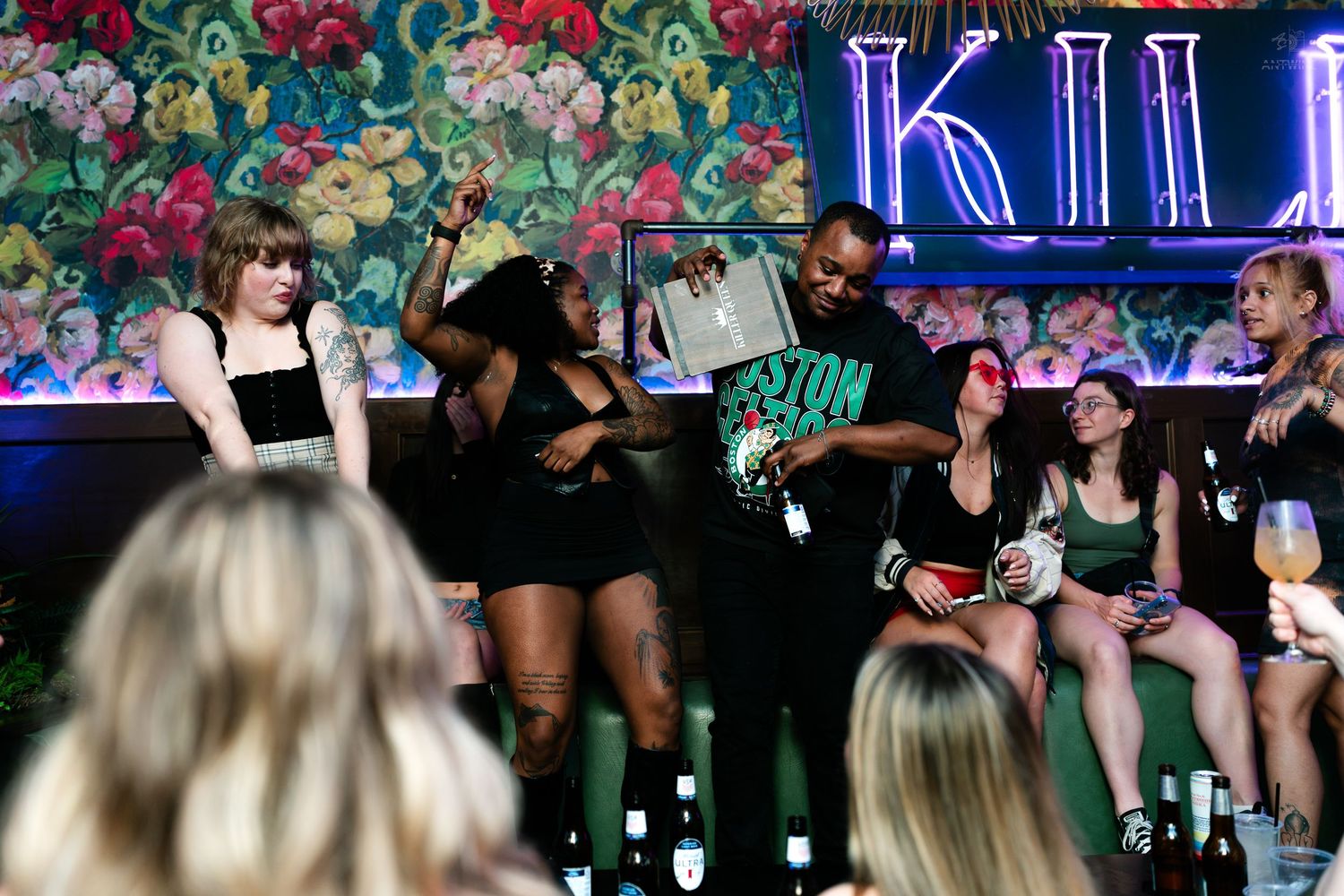 Group of people socializing at a vibrant nightclub with floral wallpaper decor.