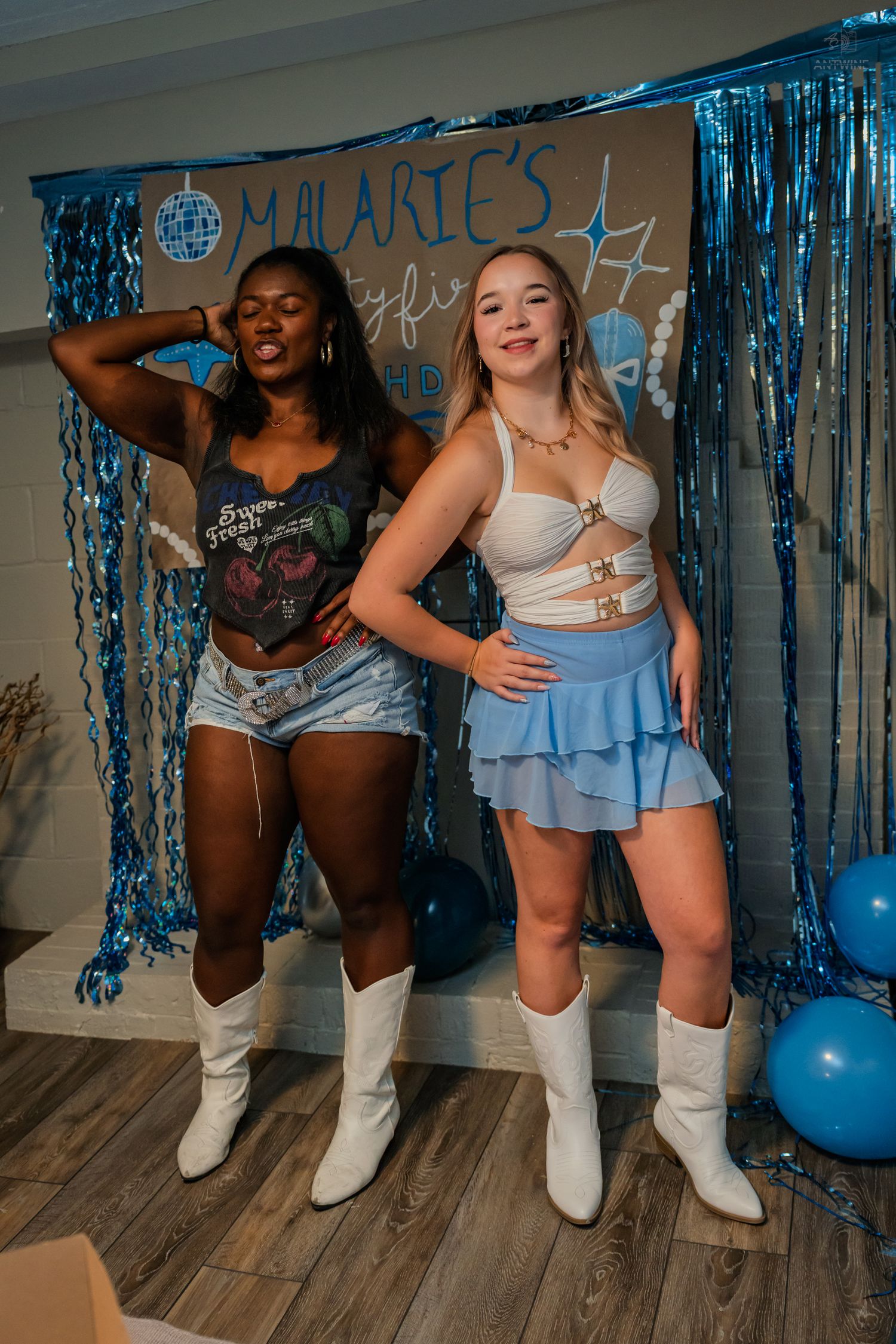 Two friends smile and pose together at a blue-themed 21st birthday celebration with tinsel backdrop.