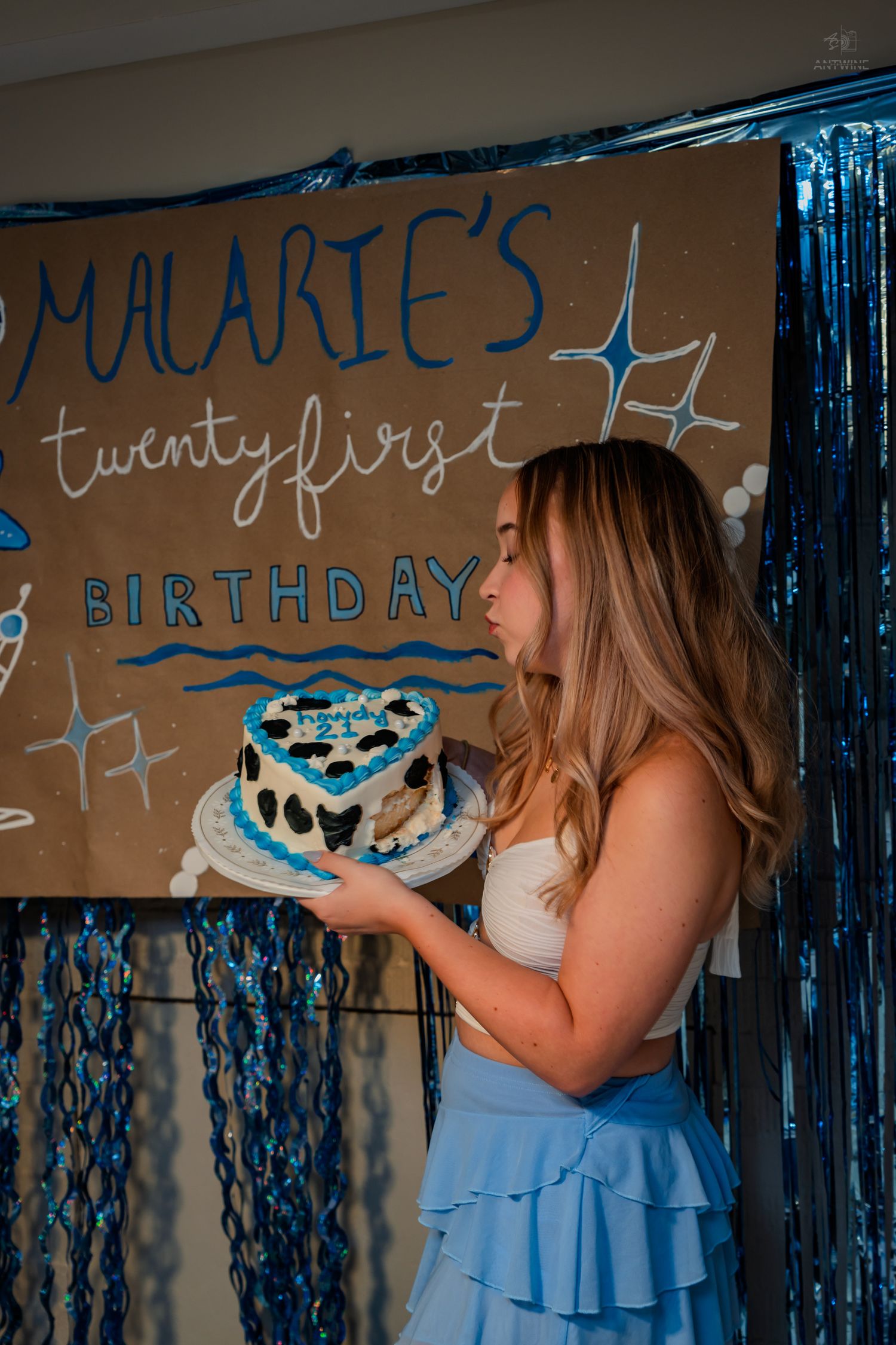 Young woman blows out candles on heart-shaped cake at Malarie's twenty-first birthday party.