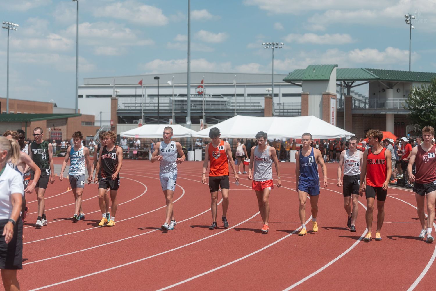 Young track and field athletes stand on a red track preparing for a race at an outdoor meet.