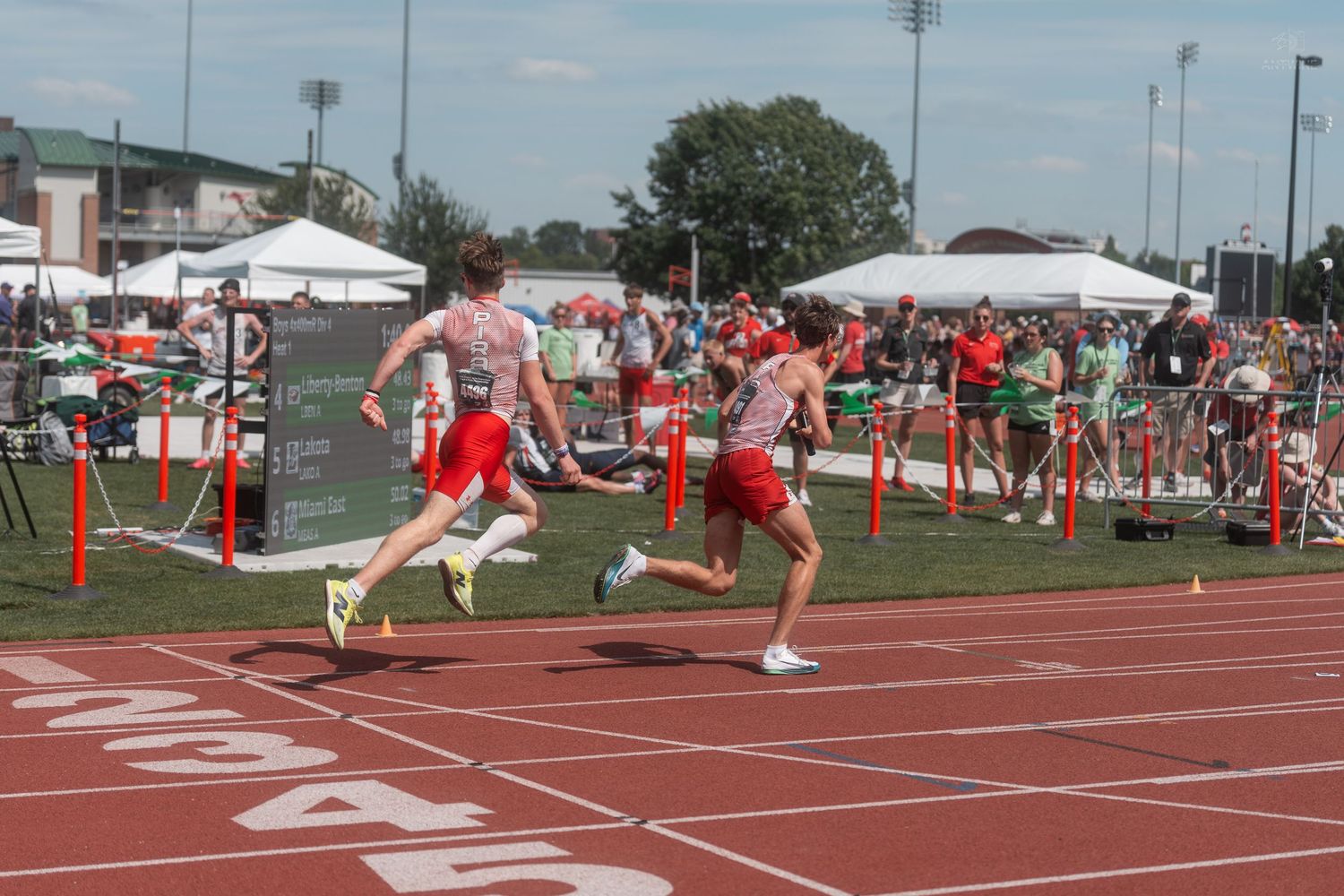 Track athletes sprint during relay race exchange zone at outdoor high school track and field meet.