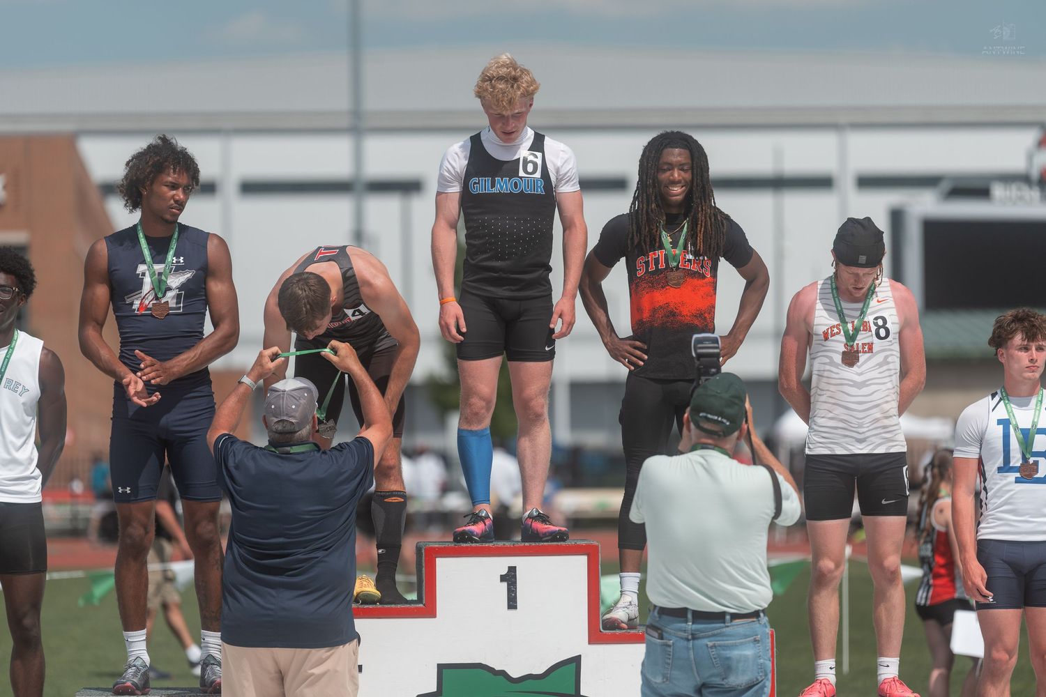 High school boys accept medals on numbered podium at sunny OHSAA track and field championship meet.
