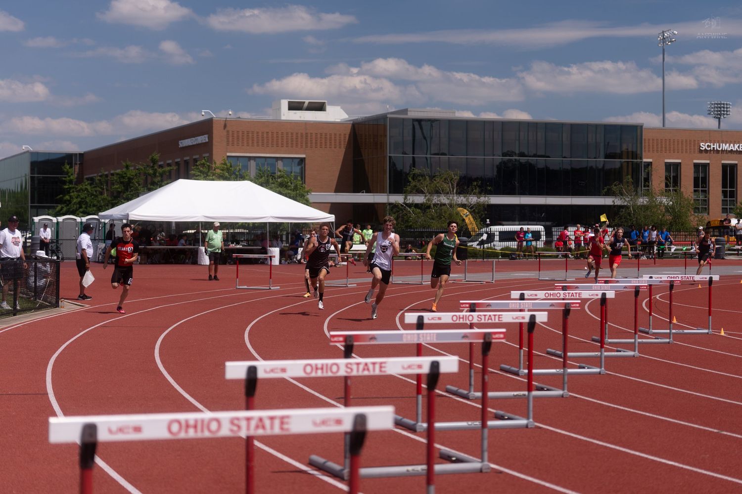 Runners clear hurdles on the Ohio State University track during a sunny high school championship track meet.
