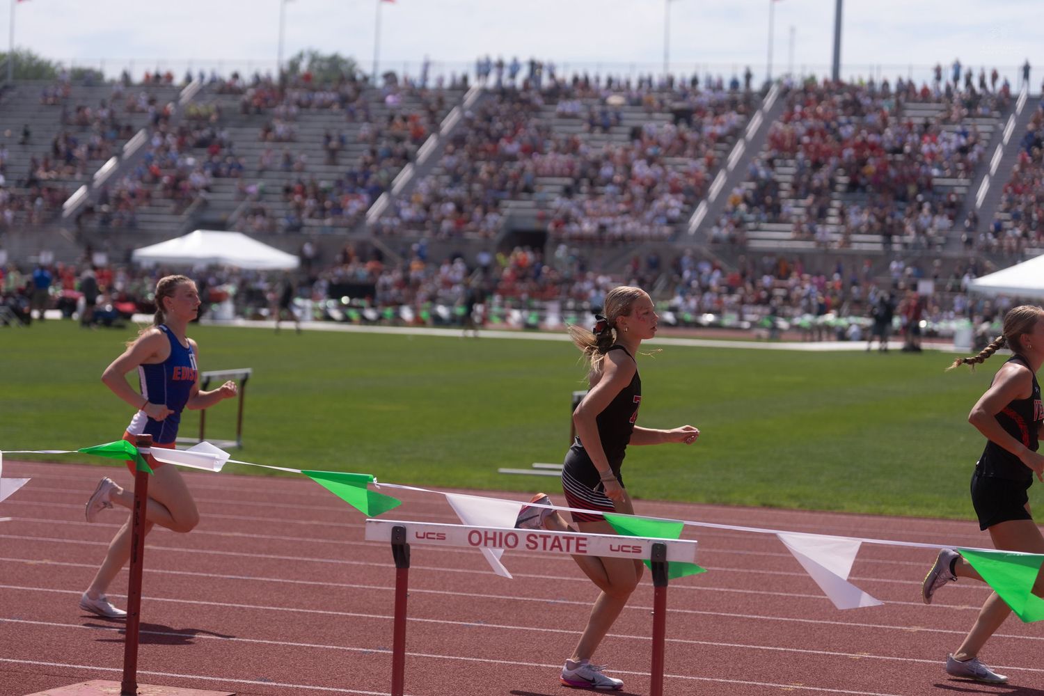 Female athletes clear hurdles during a competitive track meet at Ohio State University stadium.