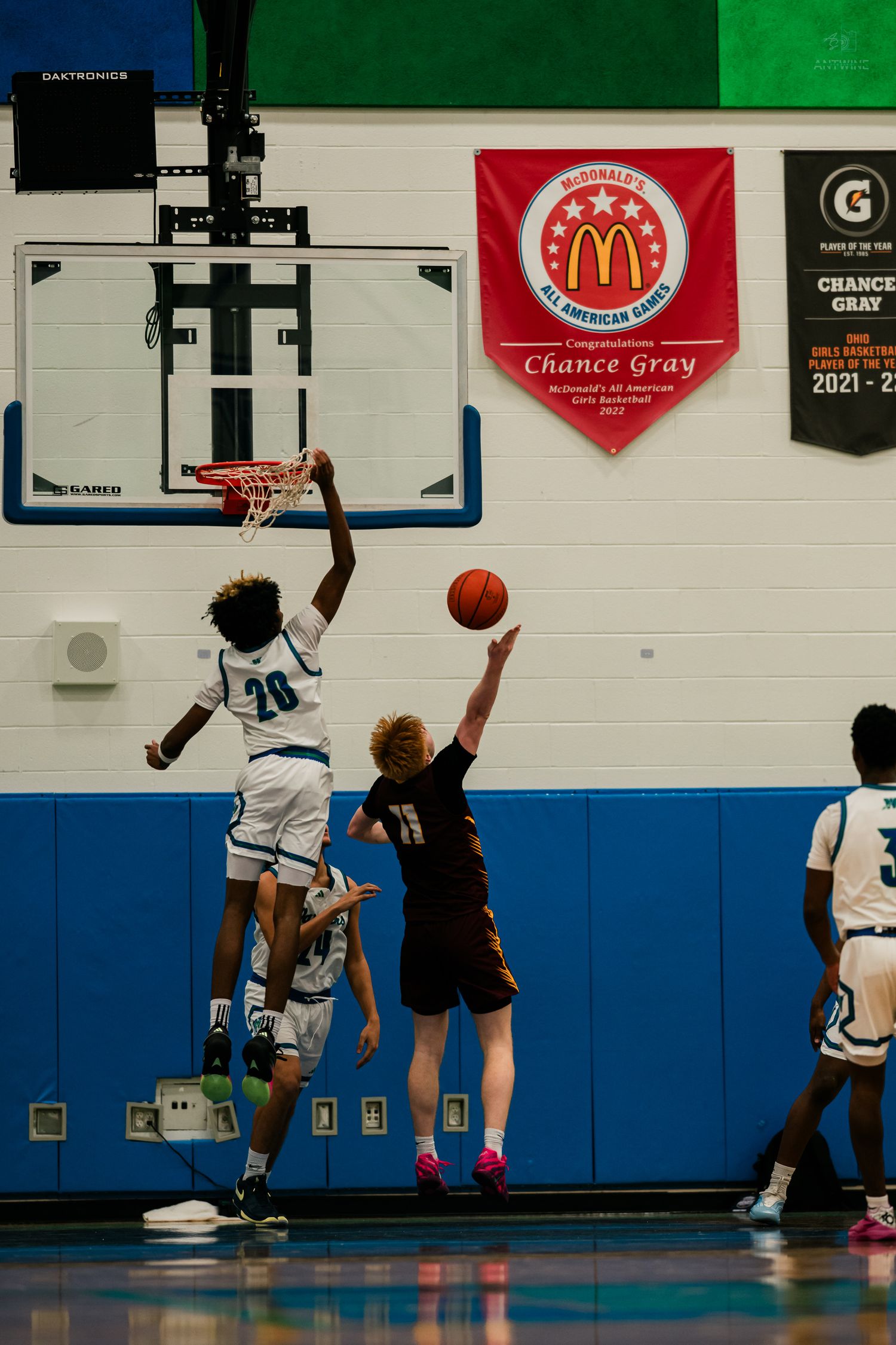 Warriors player number 20 leaps to block a shot near the rim during an indoor basketball game.