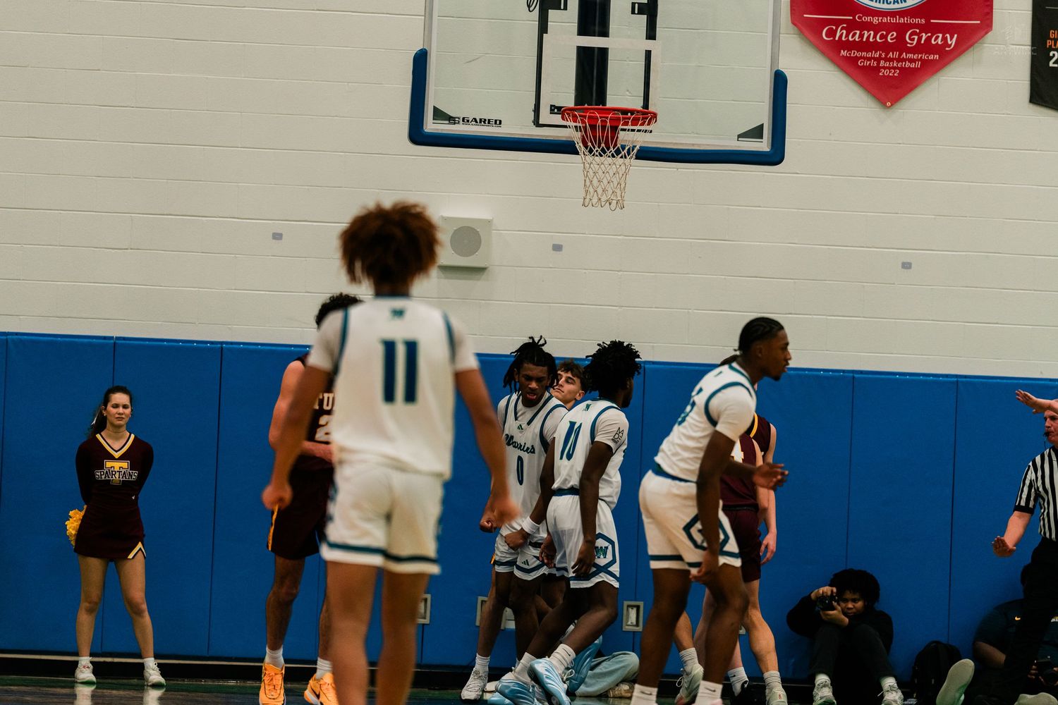 High school basketball players in white Warriors uniforms huddle near the hoop during an indoor game.