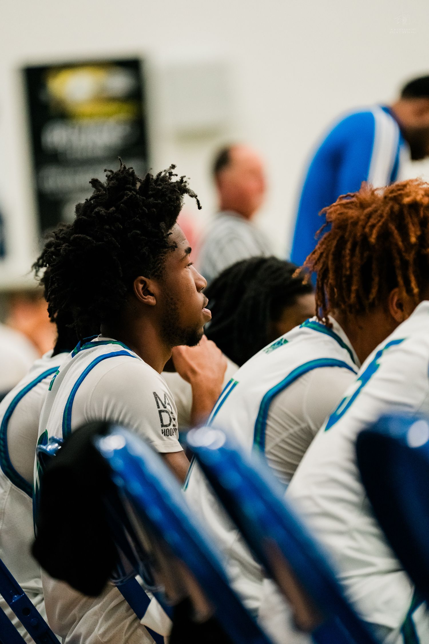 Basketball player sits on bench in white and blue uniform during a game.