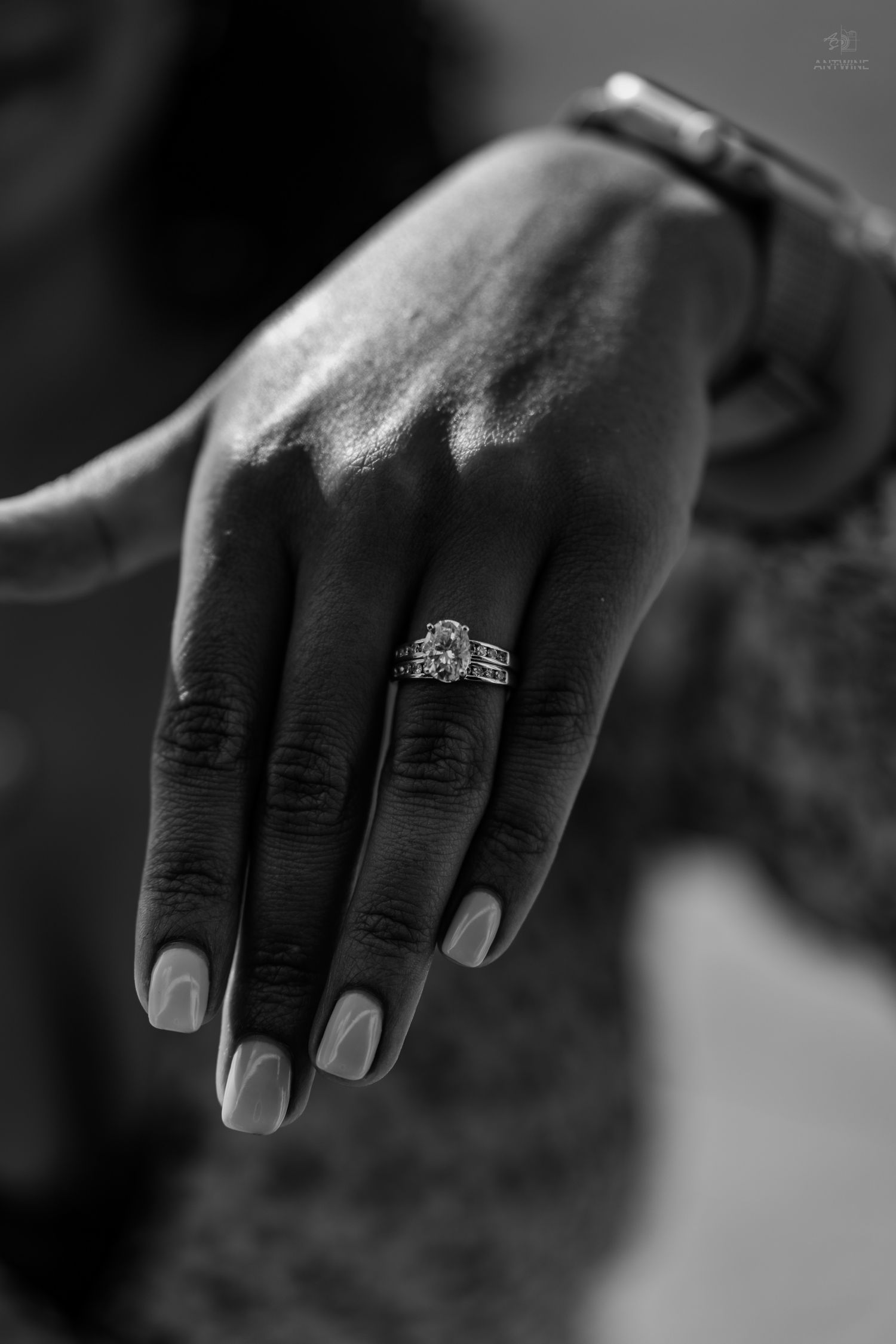 Black and white close-up of a woman's hand showcasing a beautiful diamond engagement ring on her finger.