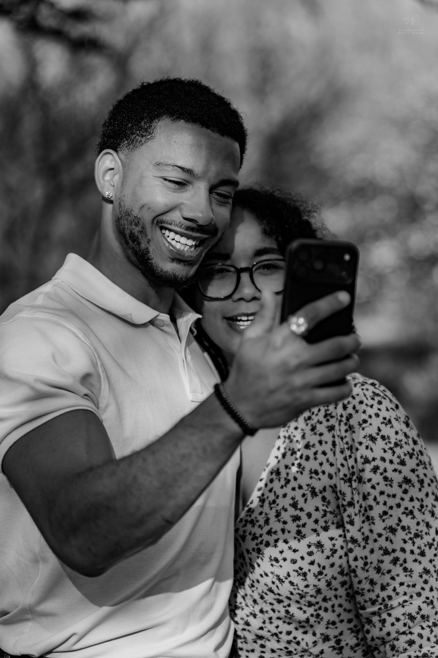 Black and white photo of happy couple taking a selfie outdoors, both smiling and leaning close together.