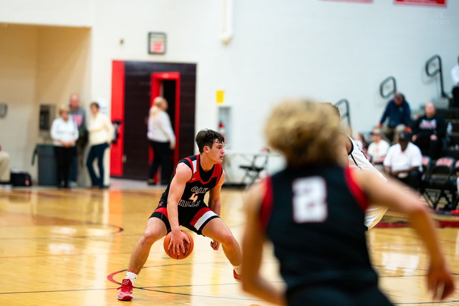 Young basketball player in red and black uniform dribbles low while a teammate in number 2 jersey stands nearby.