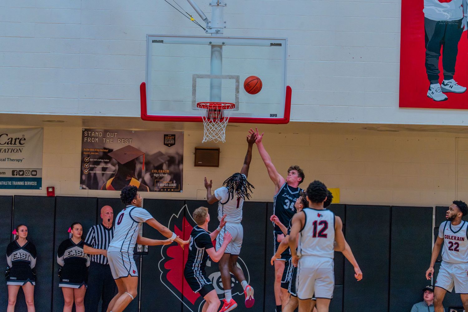 High school basketball players compete for a rebound near the basket during an indoor game.