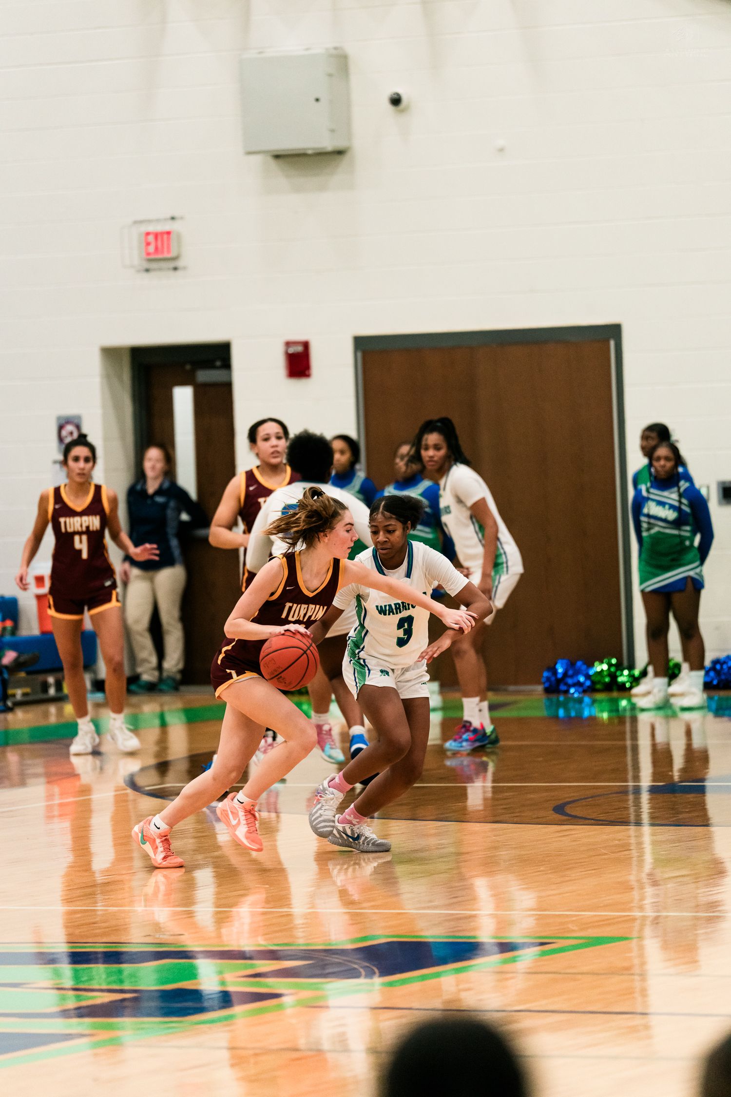 A maroon-uniformed girls basketball player drives past a Warriors defender number 3 during a high school game.