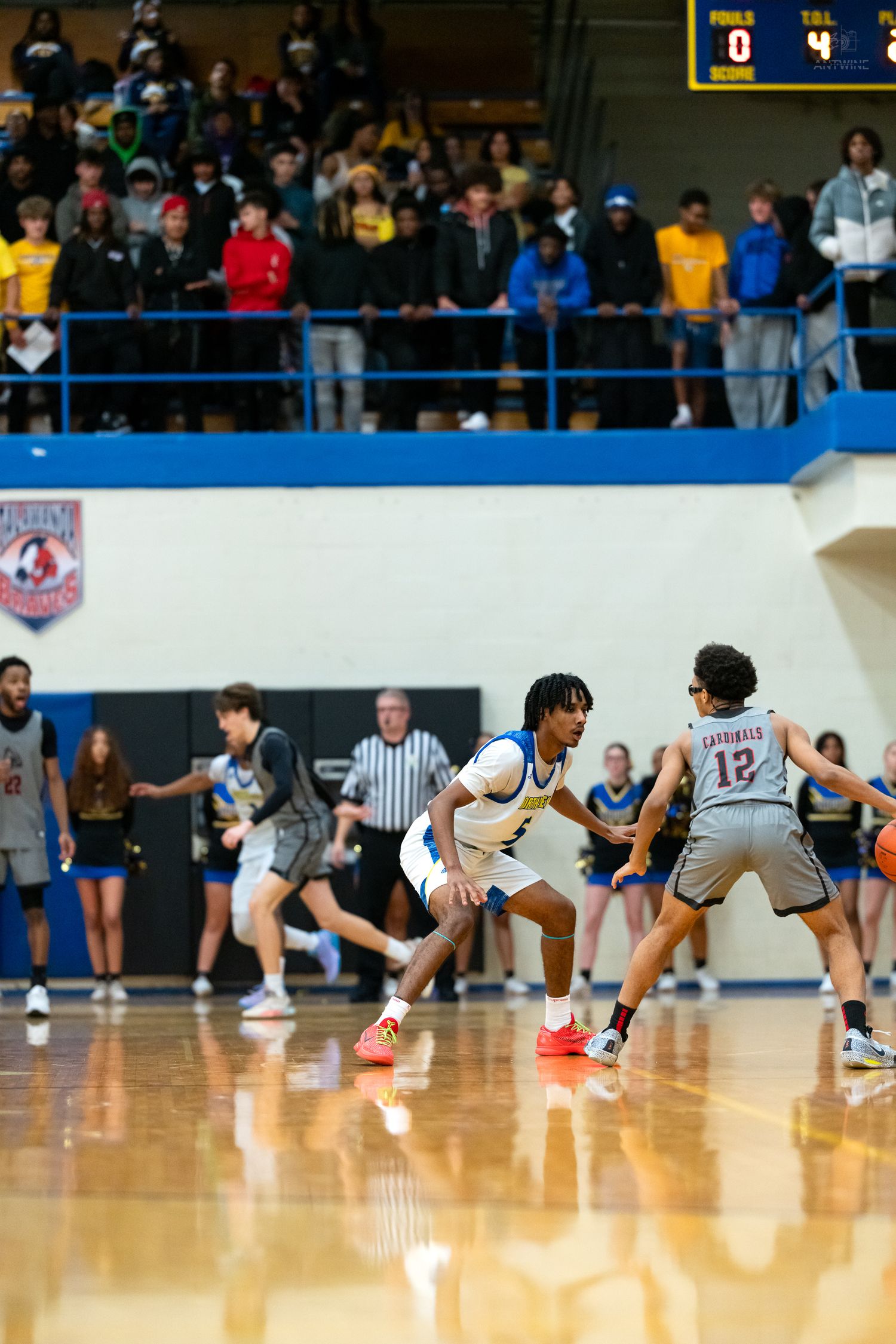 Blue team defender guards Cardinals #12 during intense high school basketball game with full crowd.