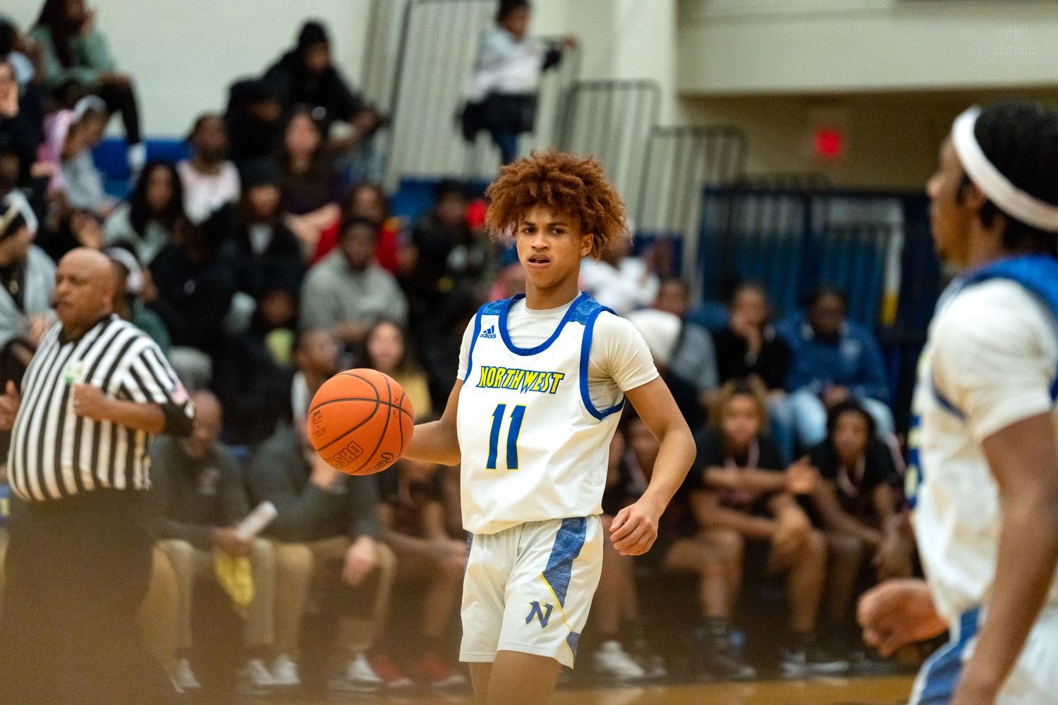 High school basketball player #11 dribbles the ball up the court during a competitive game.