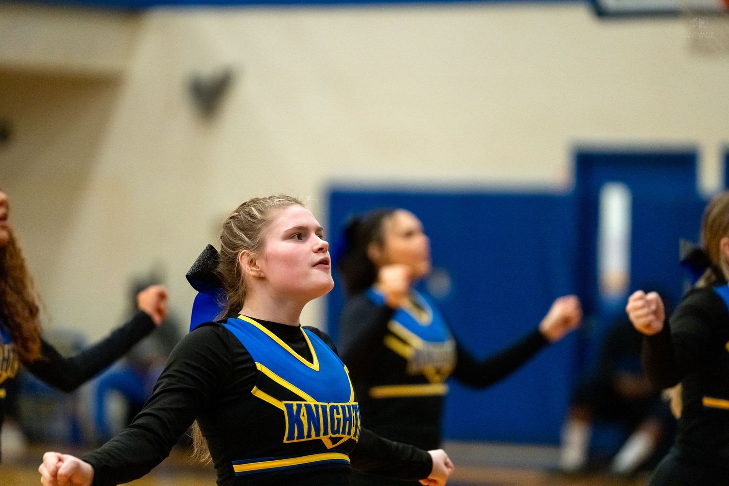 Knights cheerleader in black and blue uniform performs cheer routine during basketball game.