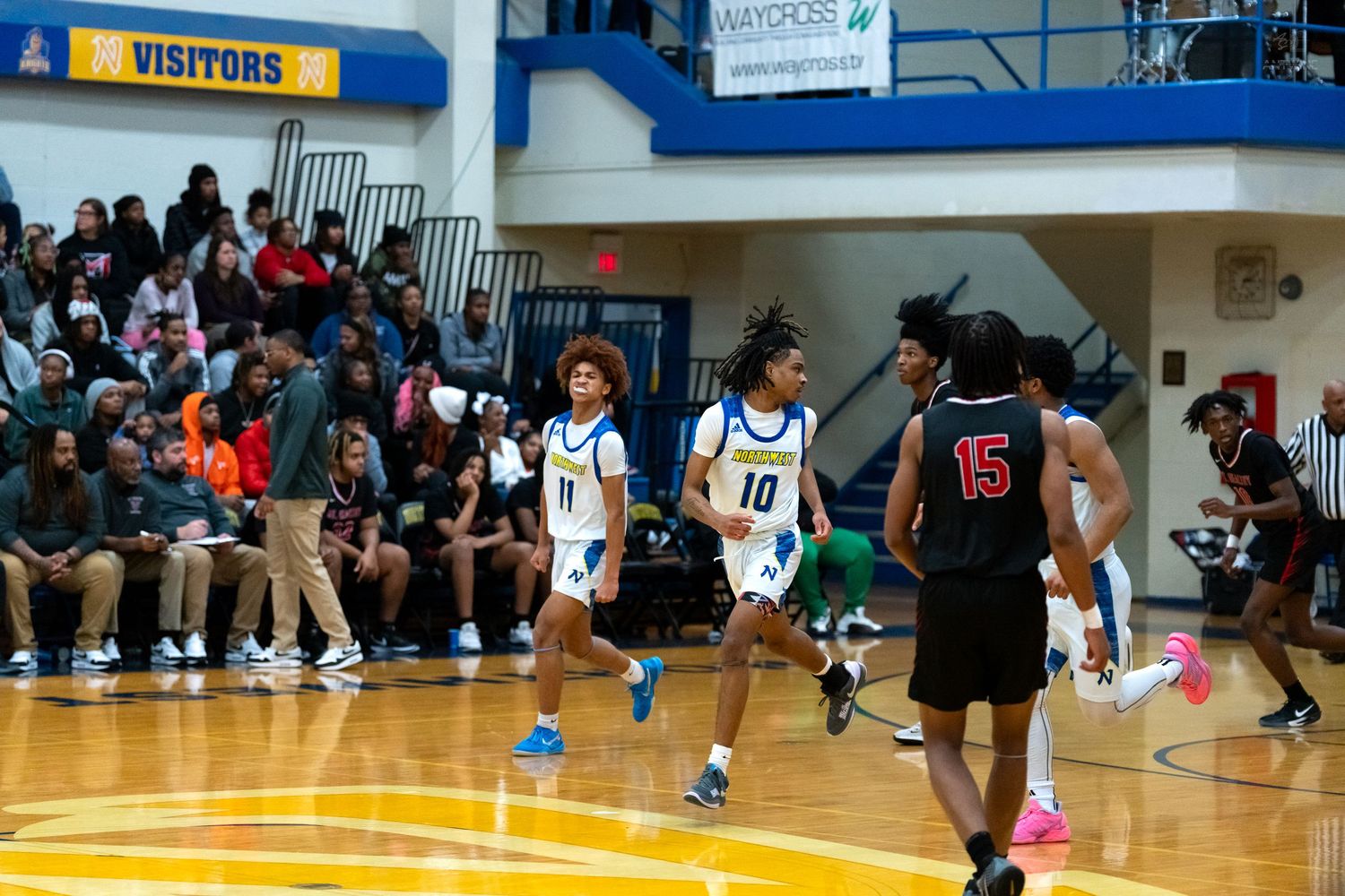High school basketball players #10 and #15 in opposing uniforms compete on court before large crowd.