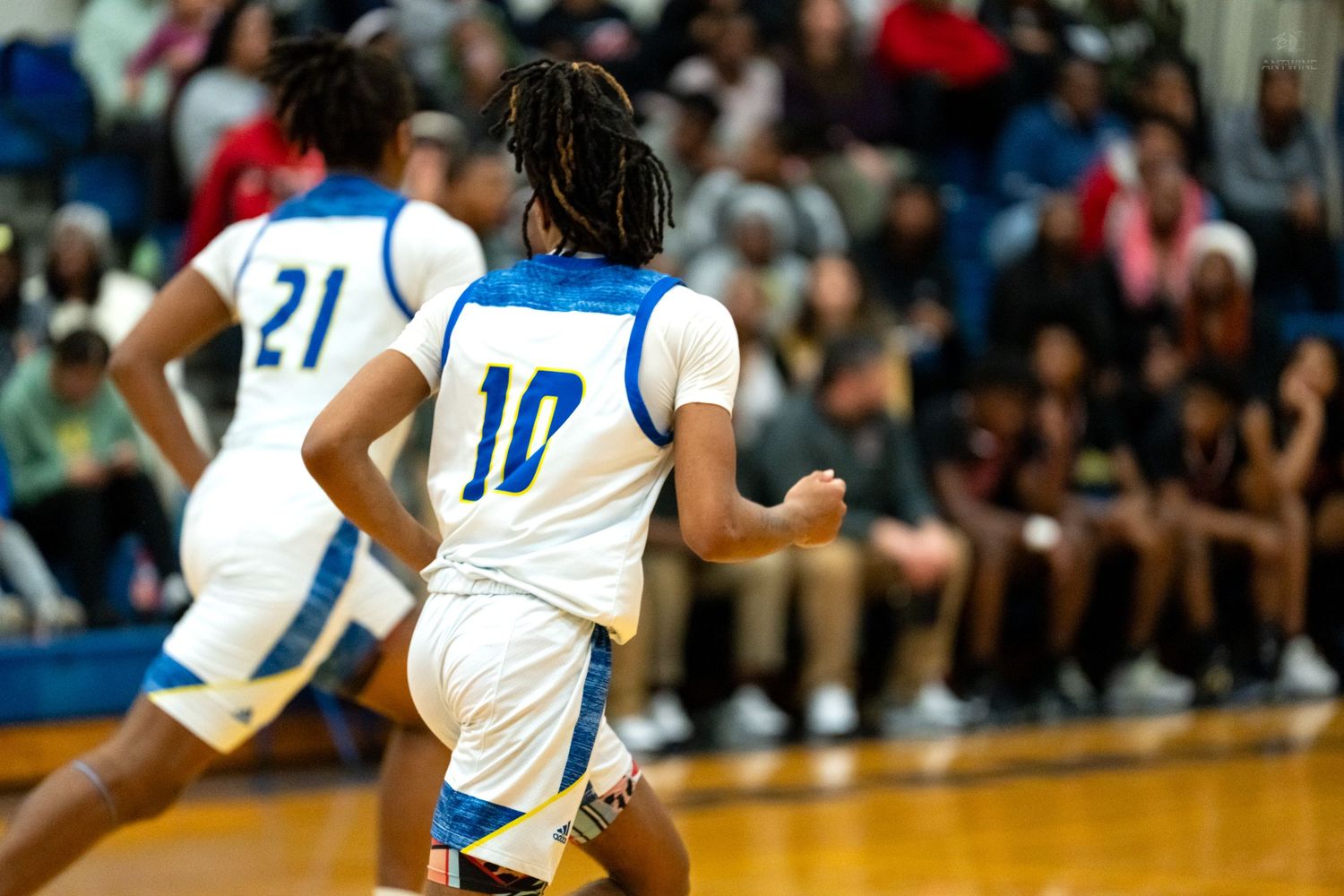 Two blue jersey players including number 10 run downcourt during a high school basketball game.