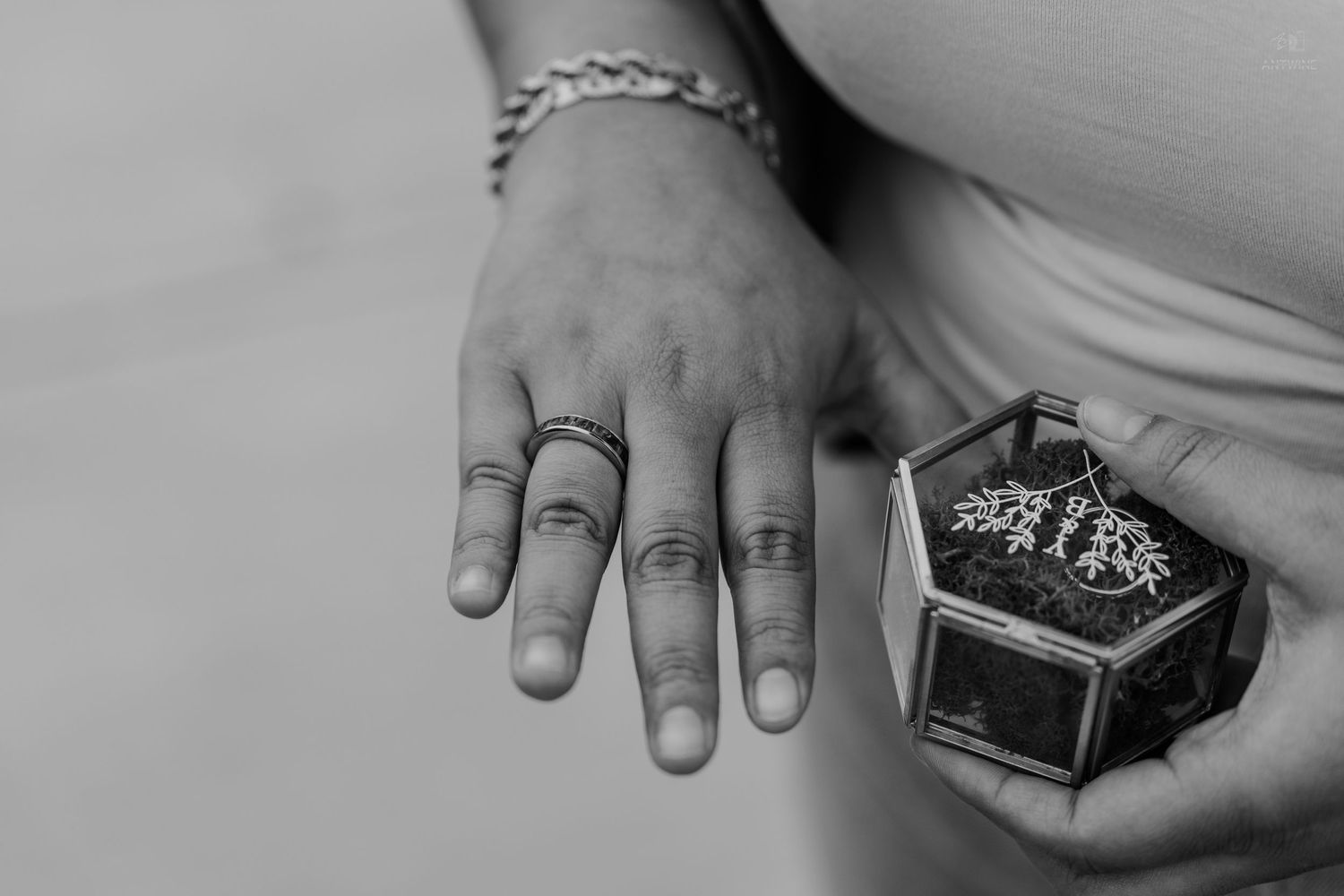 Black and white image of a hand with rings beside a small hexagonal glass jewelry box.