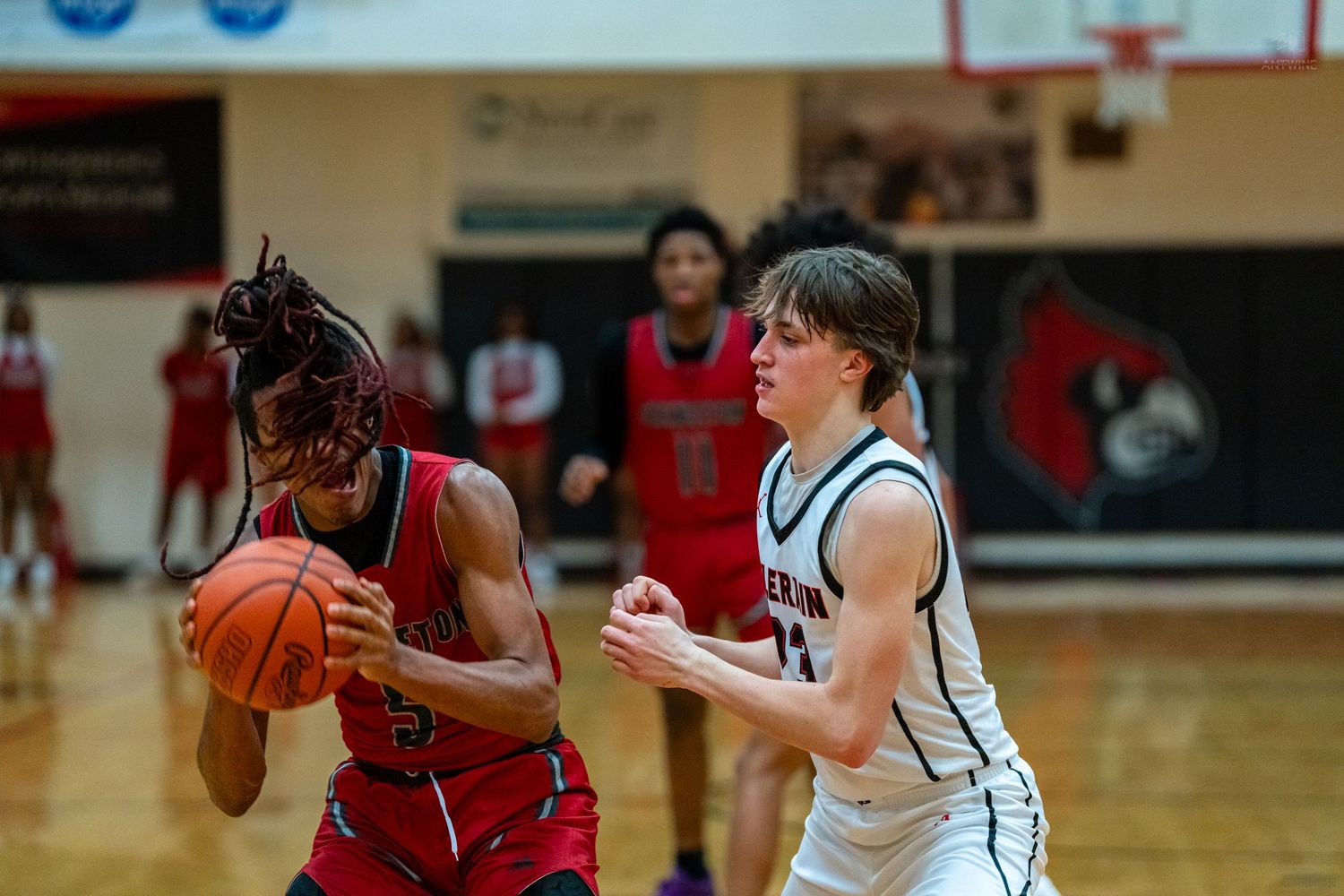 High school basketball player in red drives past a defender in white during a competitive game.