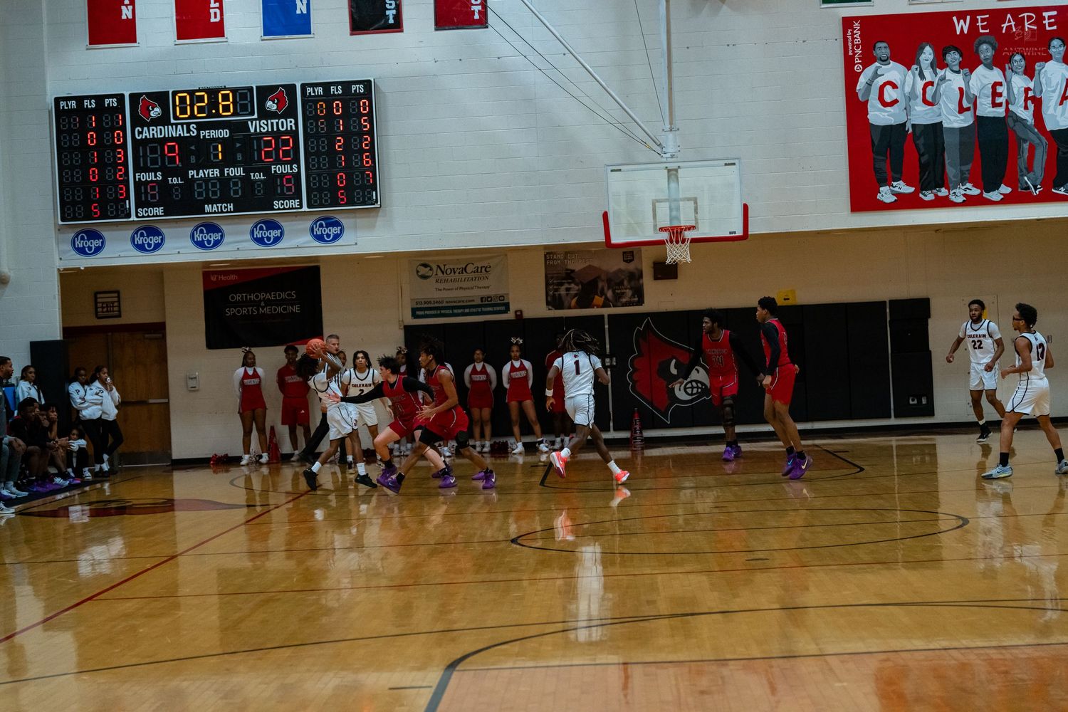 Wide shot of a high school basketball game in progress on an indoor court with scoreboard visible.
