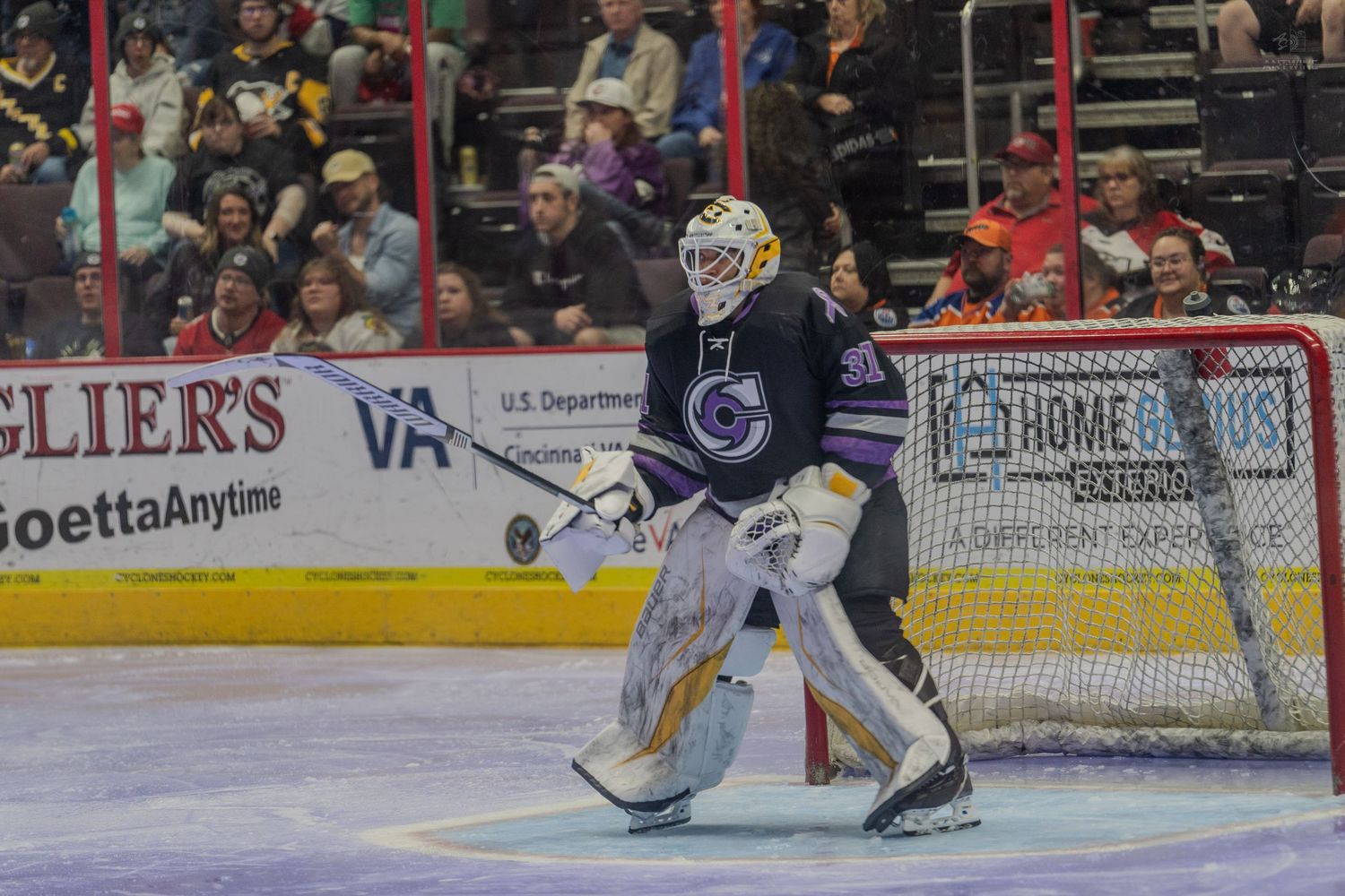 Professional hockey goalie in dark uniform guarding the net during a minor league hockey game.