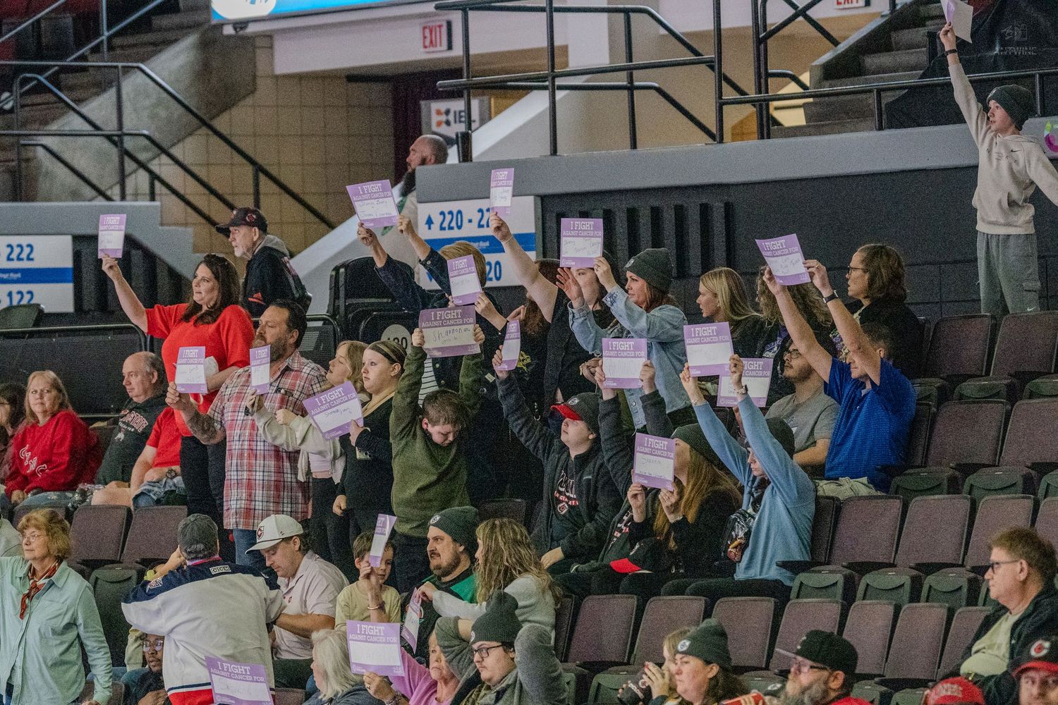 Excited hockey fans in arena stands hold up pink cards and cheer during a live game event.