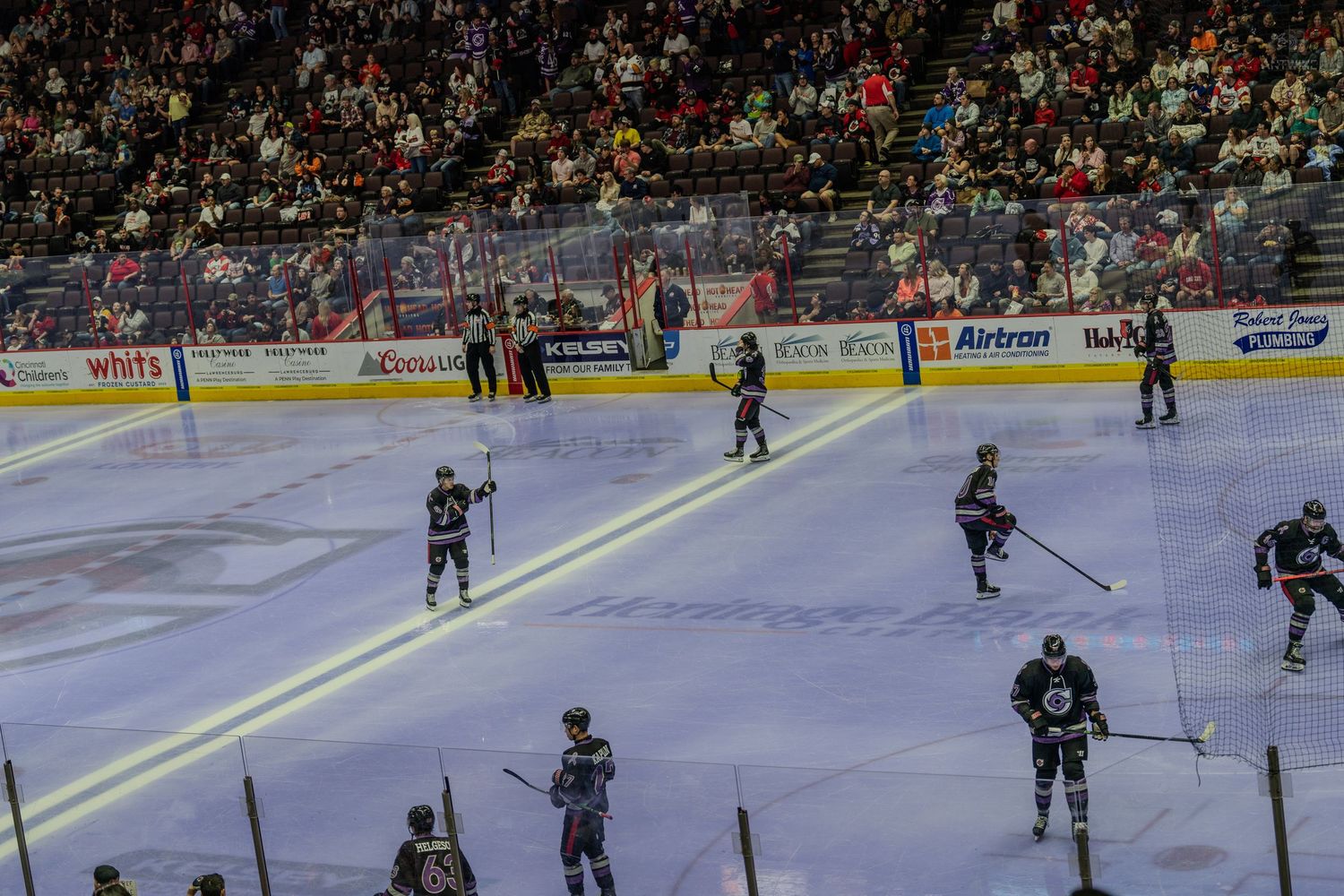 Hockey players warm up or skate during a break in play on the ice at a crowded indoor hockey arena.