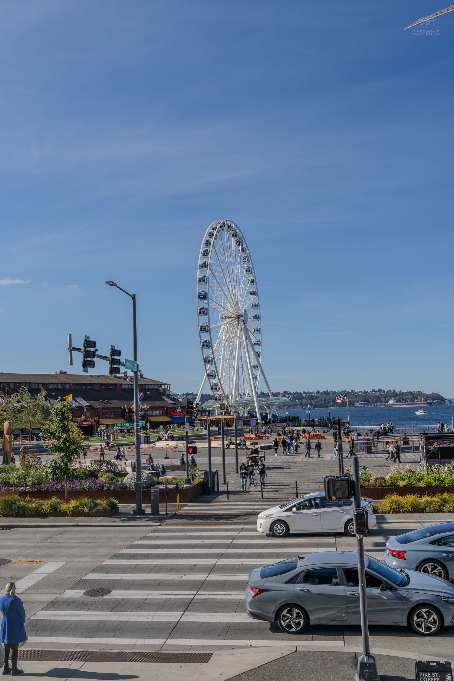 Seattle waterfront with the Great Wheel ferris wheel towering over Alaskan Way on a sunny day with blue skies.