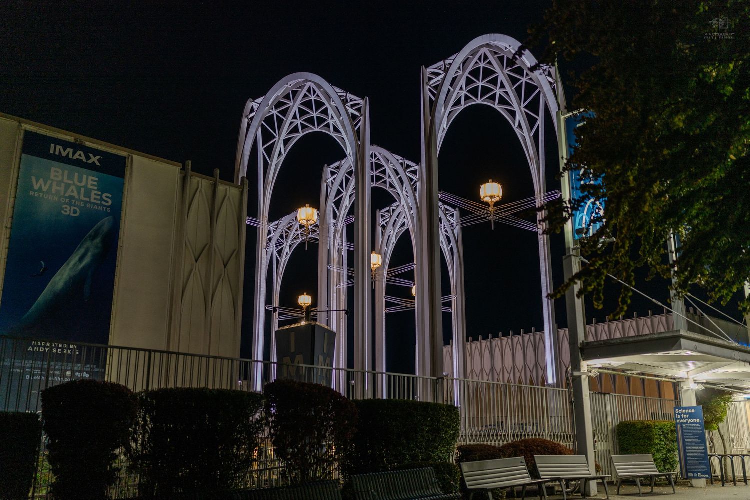 Illuminated white Gothic arch structures glow at night outside an IMAX theater with decorative lights.