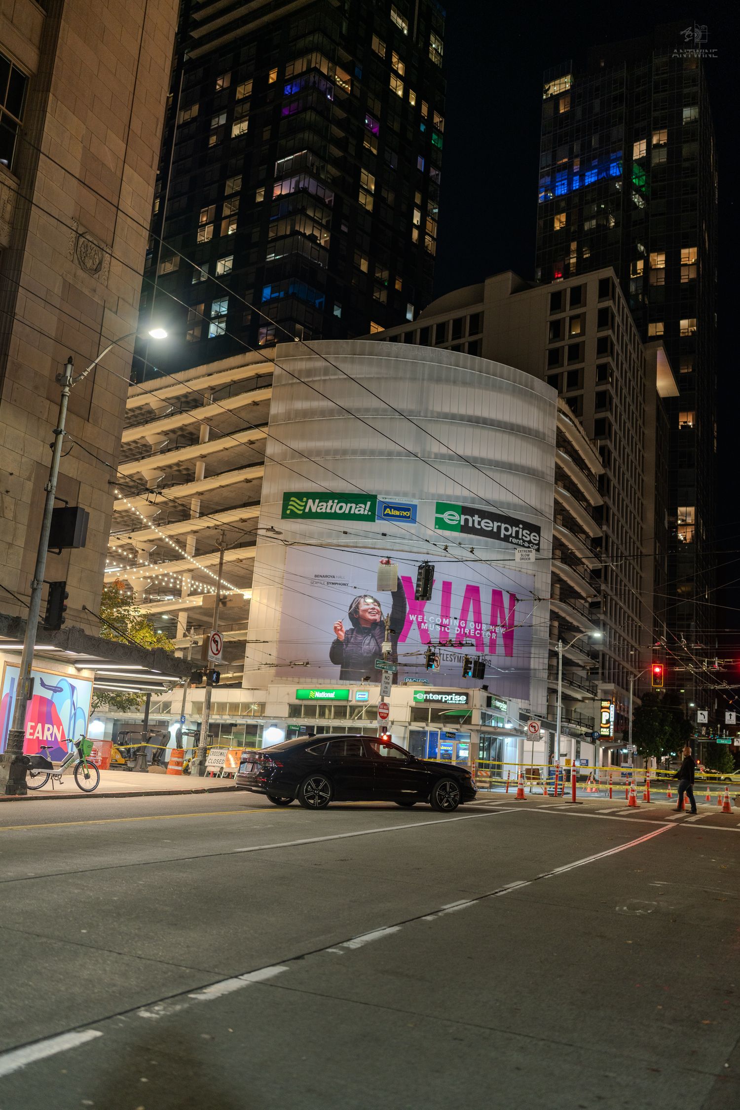 City intersection at night featuring a curved building with National and Enterprise signs and a large billboard.