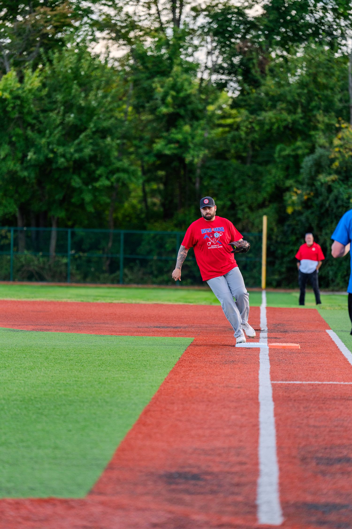 Baseball player in red uniform running bases on turf field during charity softball game.