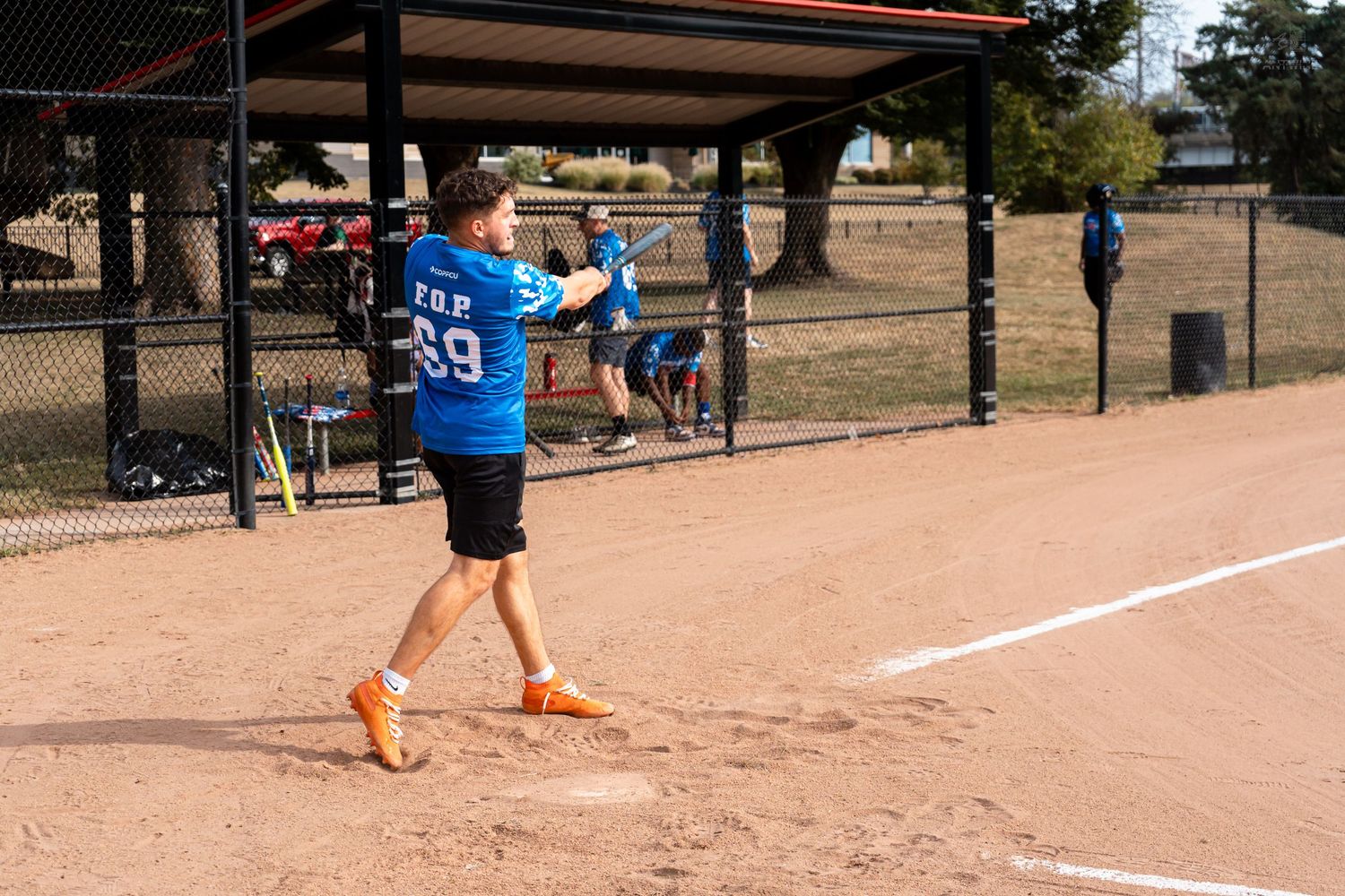 Player in blue jersey number 69 swings a bat during a softball game on a sunny dirt field.