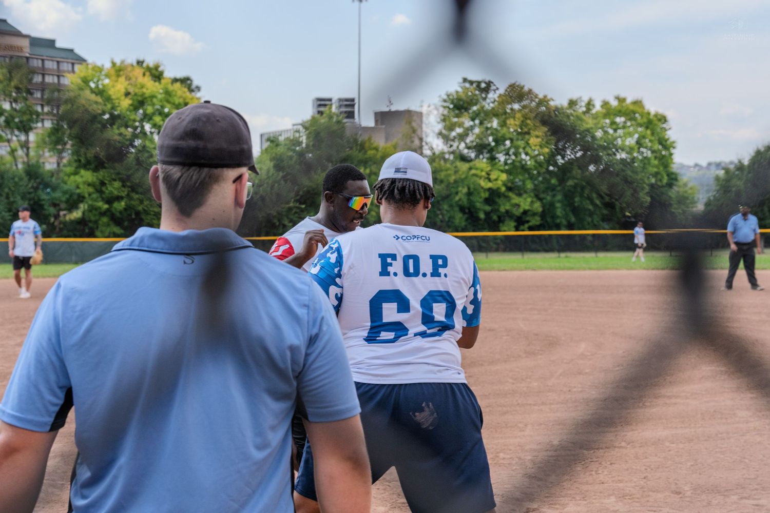 Players on a softball field wearing F.O.P. jerseys during an outdoor game on a sunny day.
