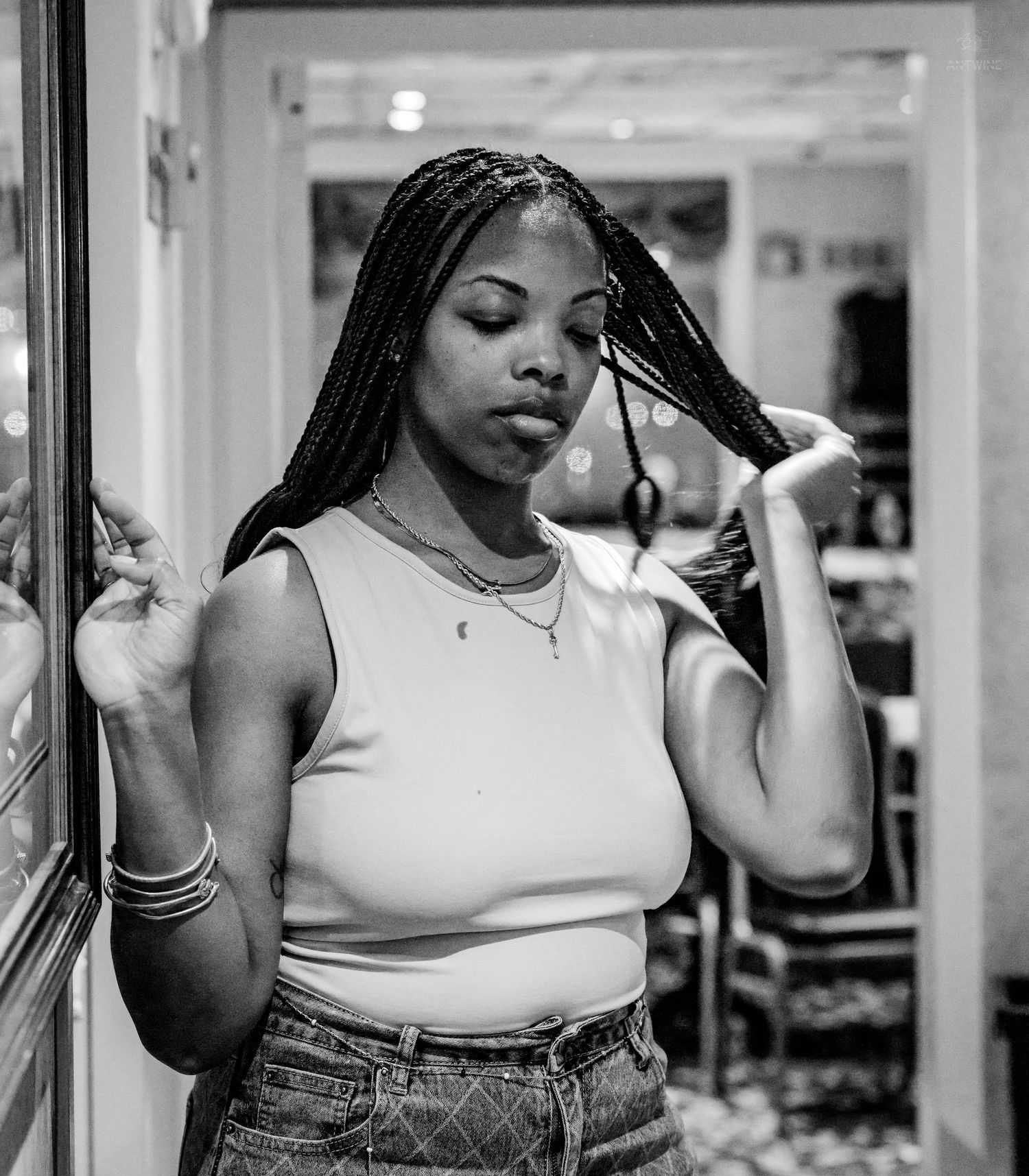 Black and white portrait of young woman with braids posing thoughtfully indoors.