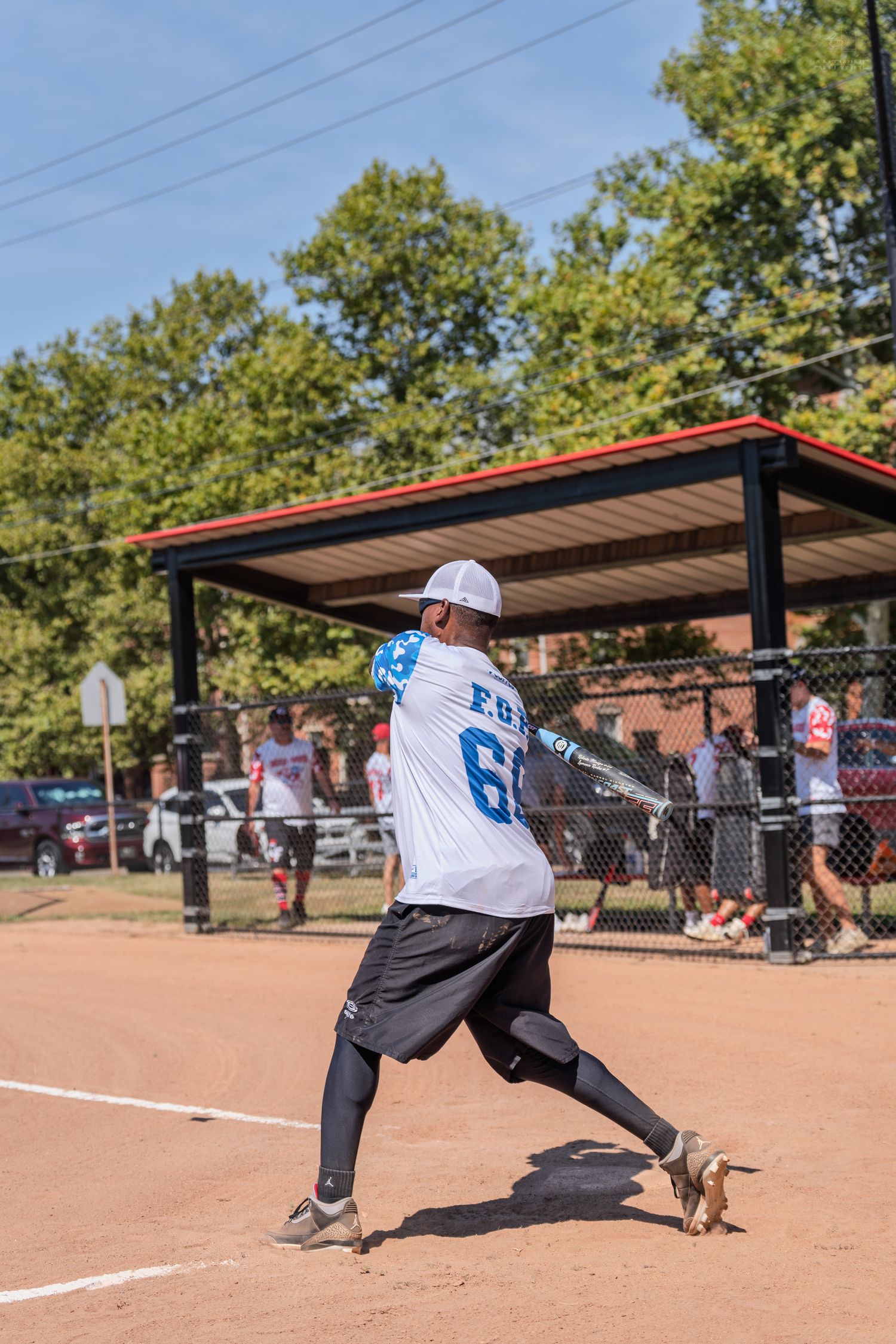 Softball player in white FOE 60 jersey swinging bat on sunny outdoor diamond.