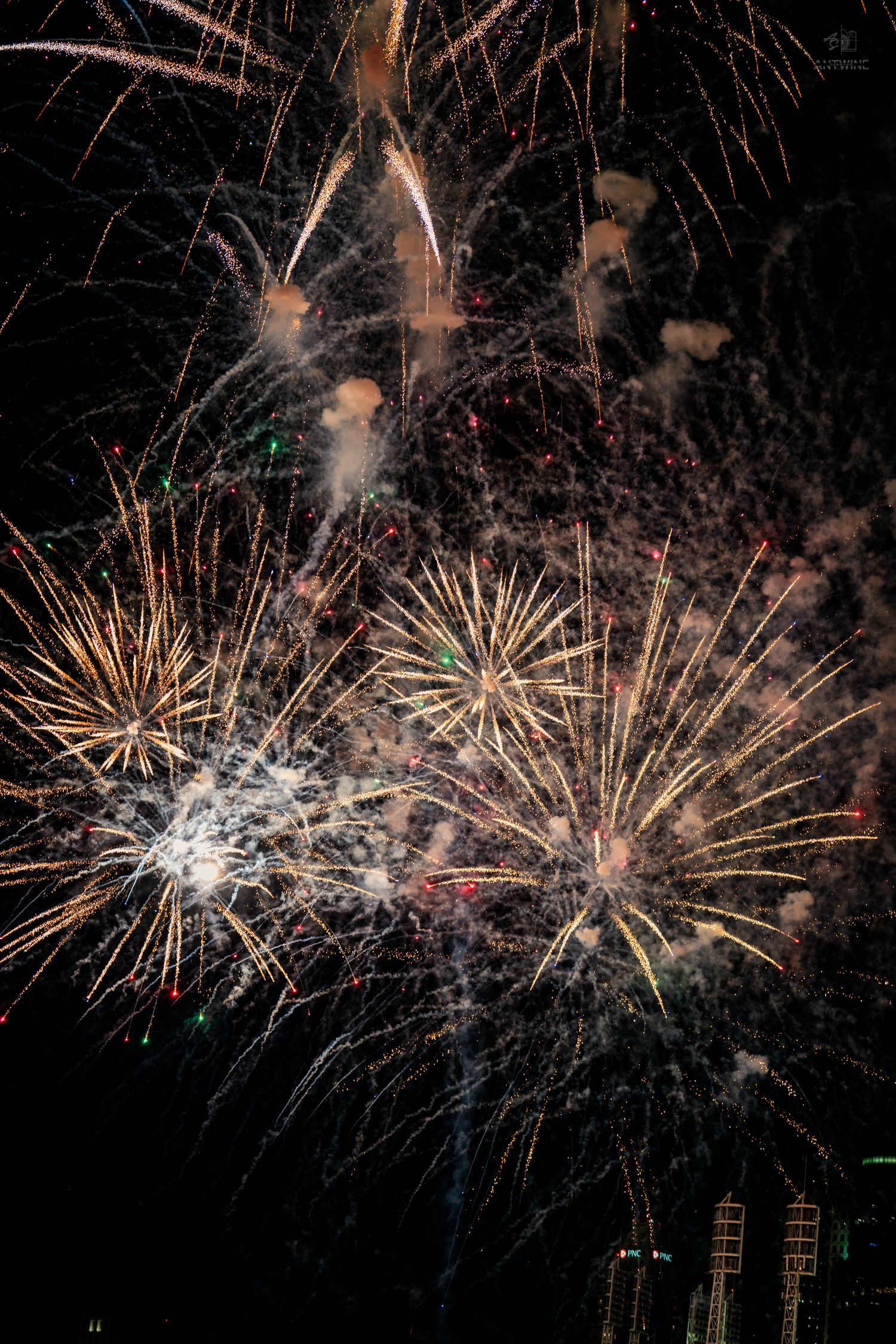 Multiple golden fireworks bursting simultaneously in the night sky above city lights.