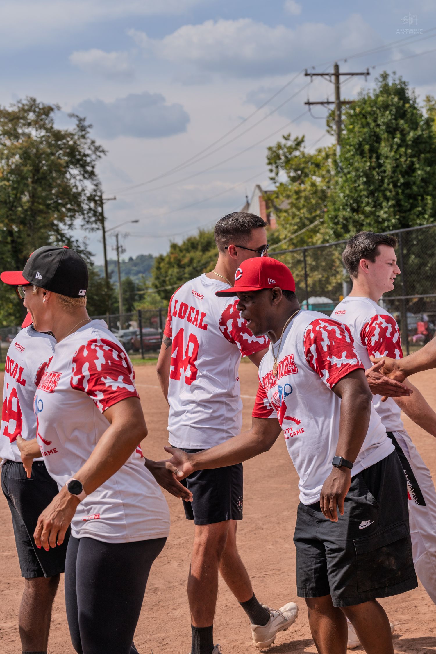 Young athletes in white and red Local 48 softball uniforms standing on a dirt field during a baseball game.