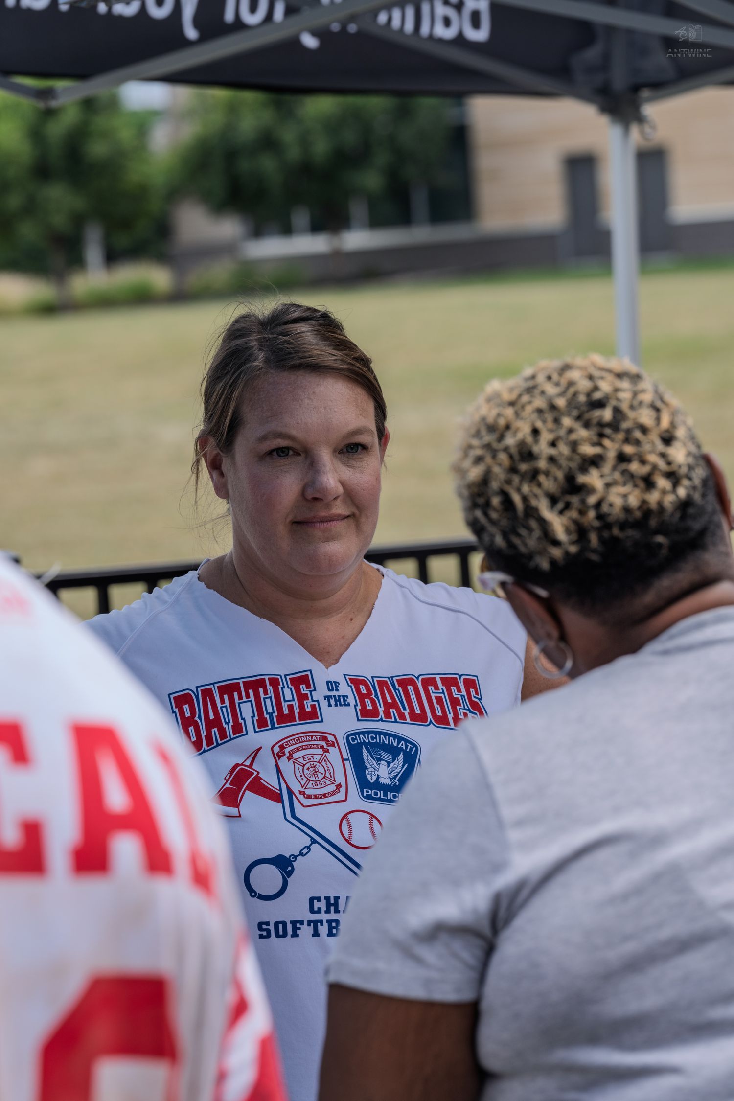 Woman in a Battle of the Badges Charity Softball white t-shirt conversing at an outdoor event.