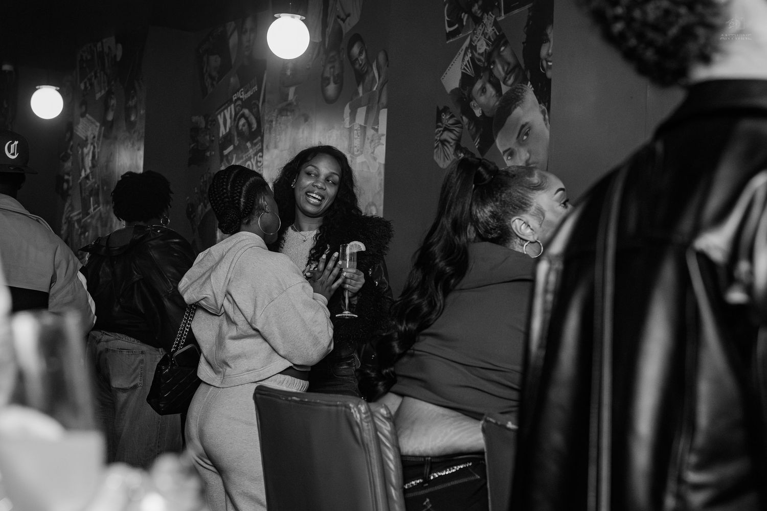 Black and white photo of women socializing at an upscale indoor party, one holding a wine glass.