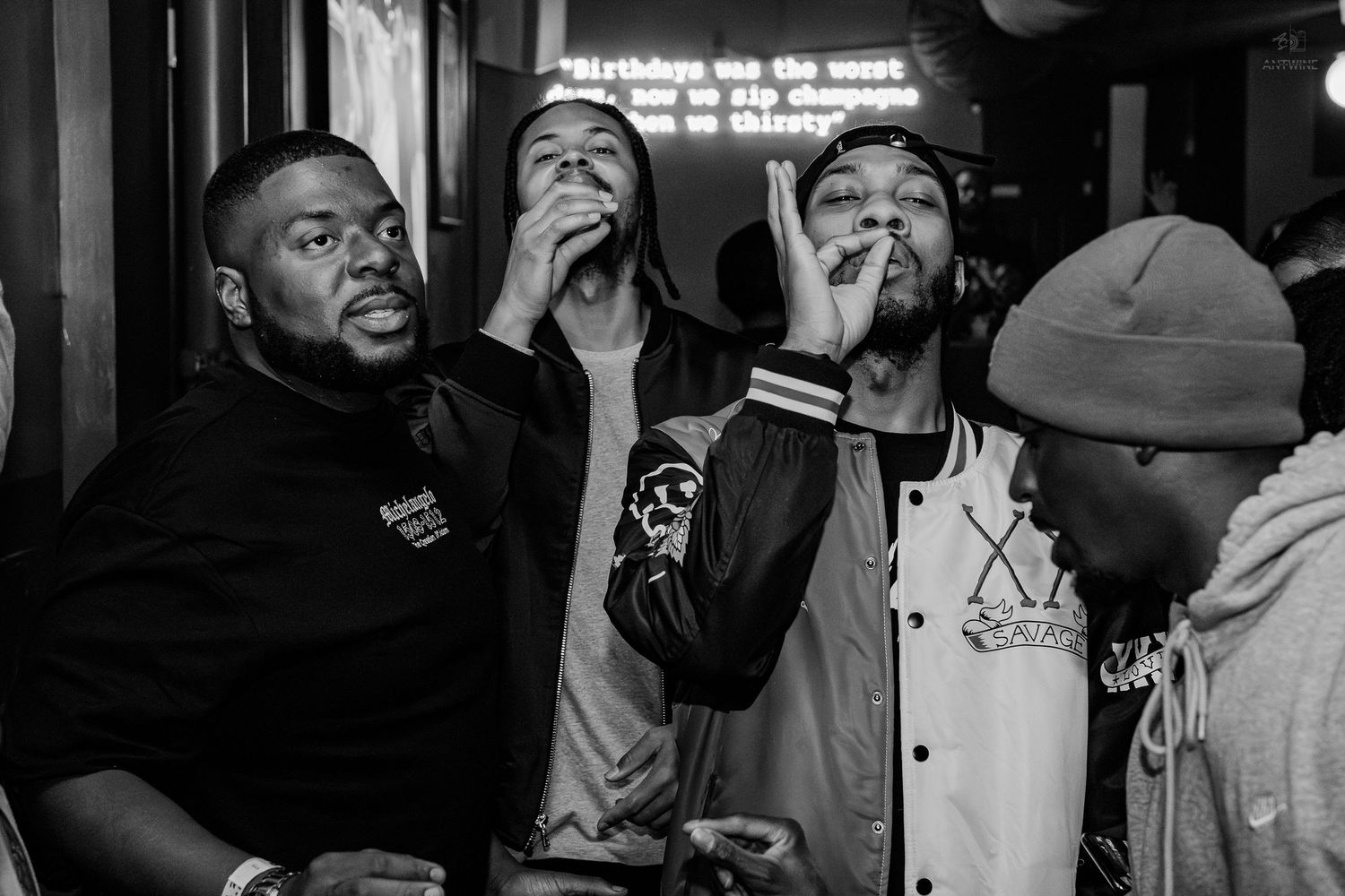 Black and white photo of four men socializing at a dimly lit bar or club event.