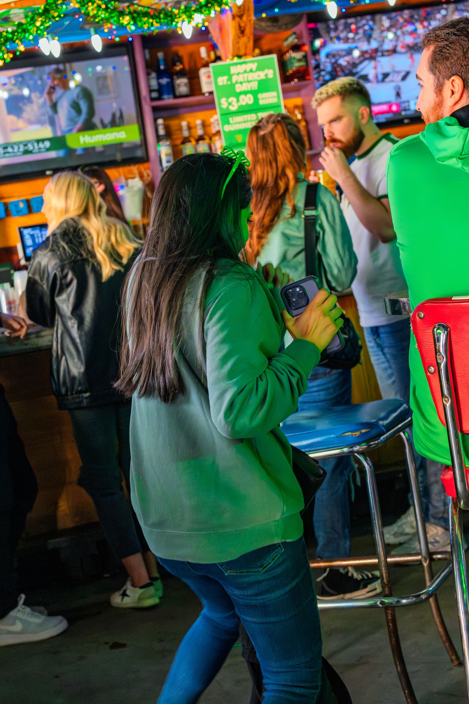 People celebrating St. Patrick's Day at a bar, wearing green outfits under colorful neon lights.