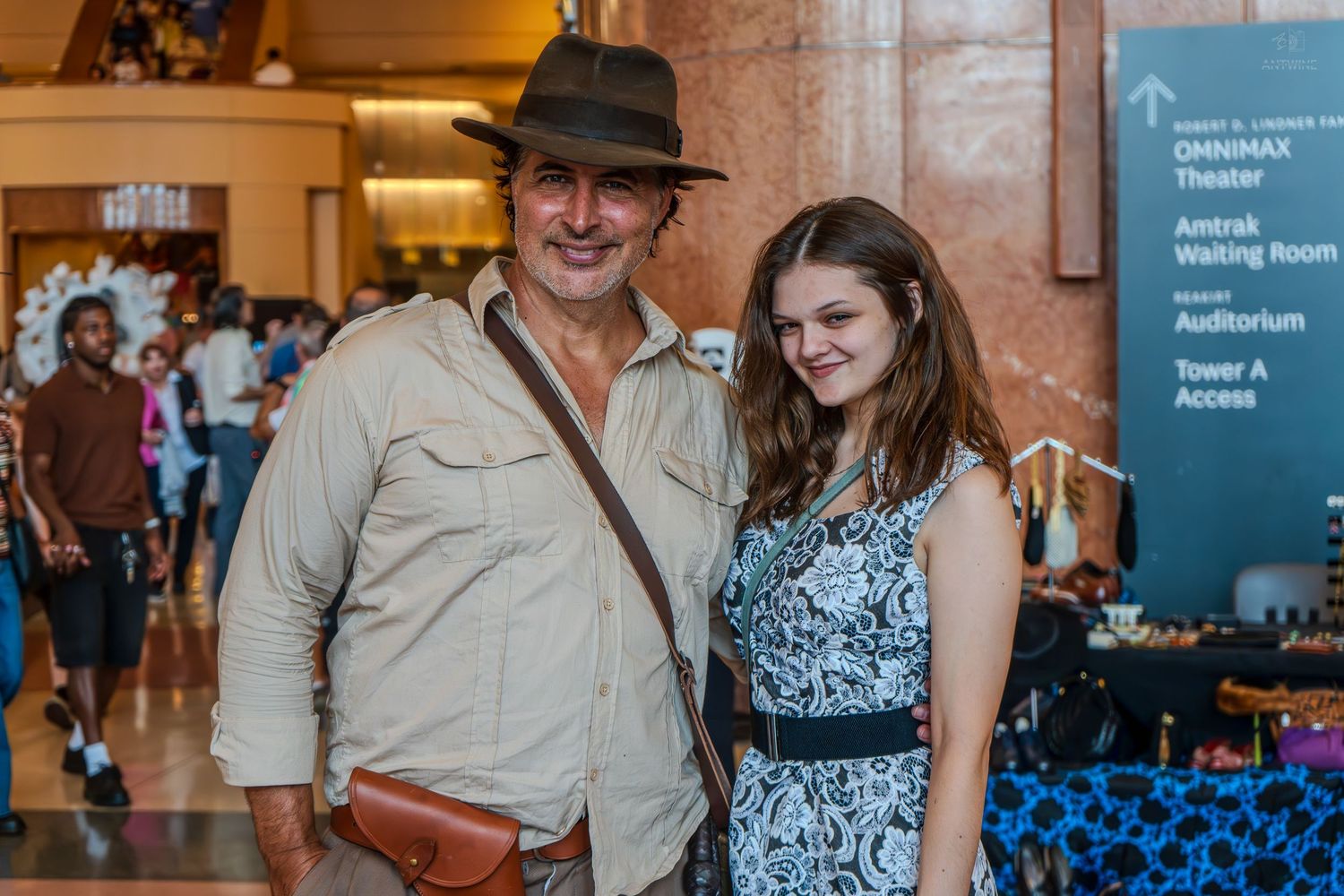 Man in Indiana Jones costume and young woman posing together at an indoor event venue.