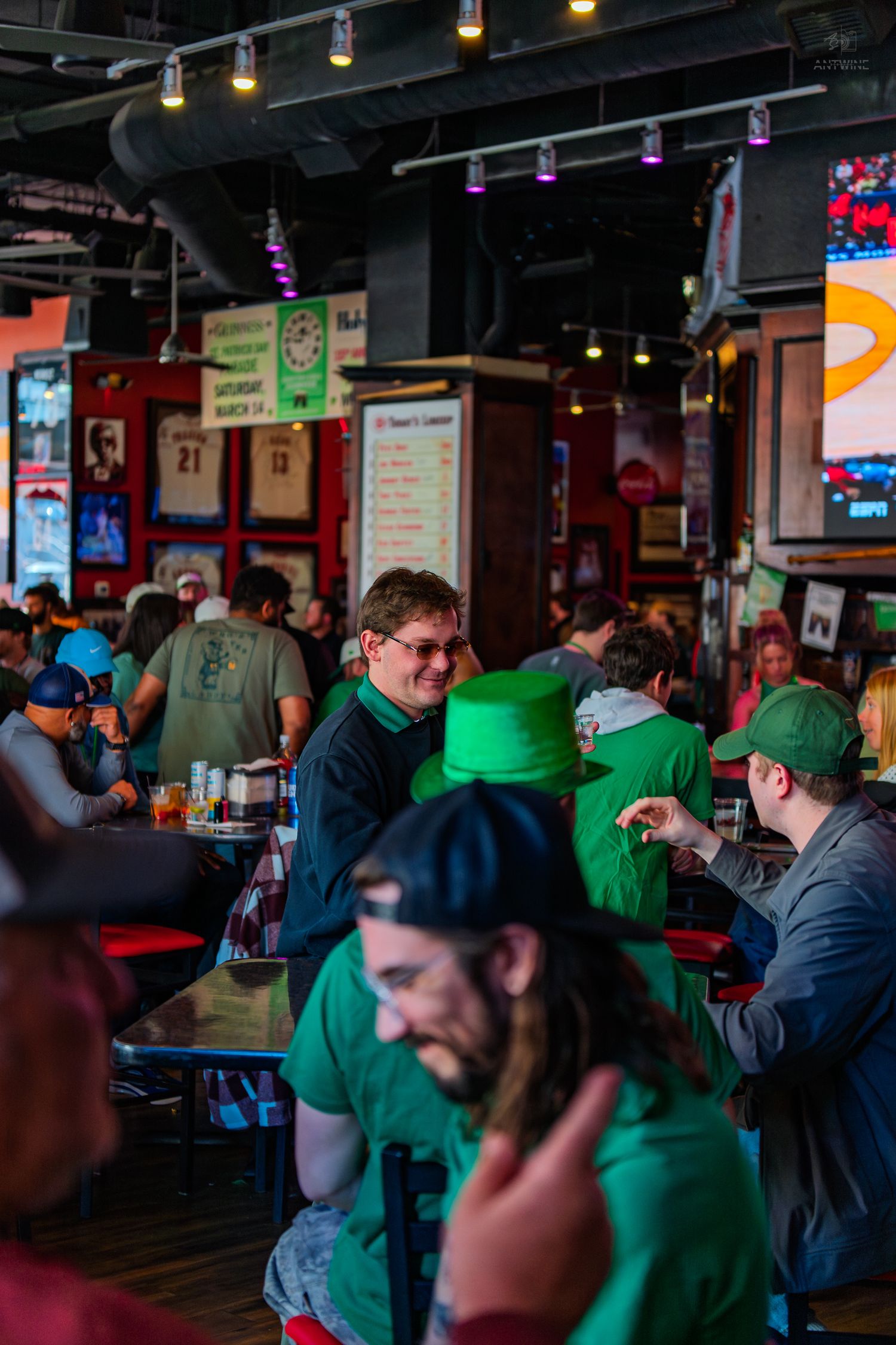 Crowded Irish bar with patrons wearing green on St. Patrick's Day, featuring sports TVs and festive decorations.