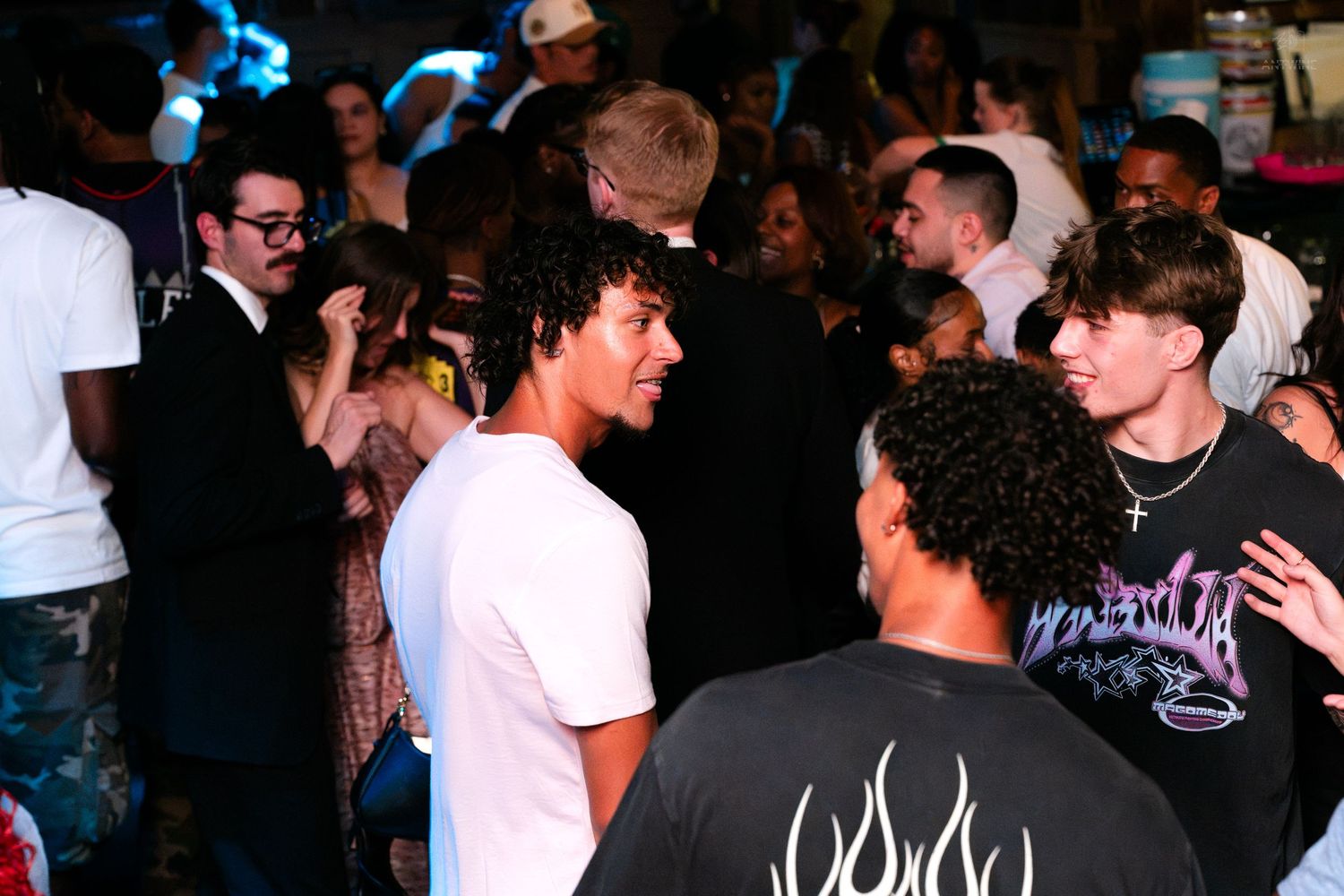 Group of young men socializing at a busy nightclub event with crowd behind them.