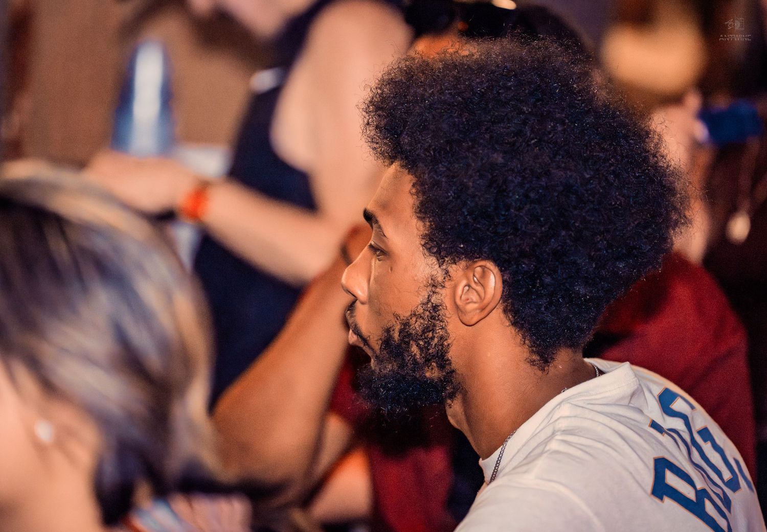 Close-up profile of man with afro hair at a crowded indoor event.