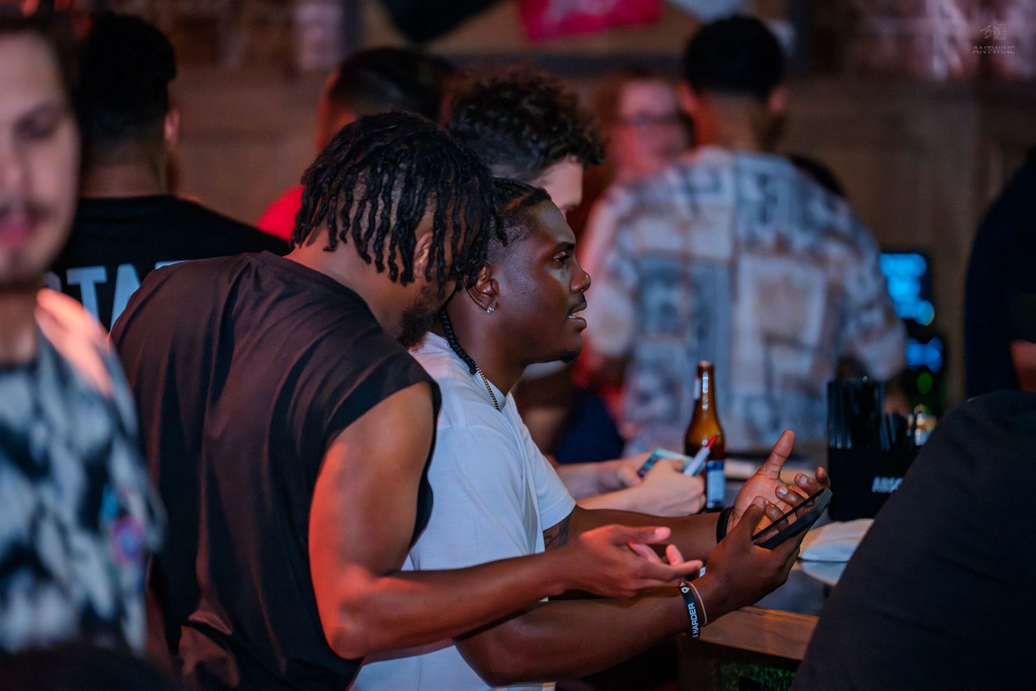 Two friends lean together watching an event at a dimly lit bar or club venue.