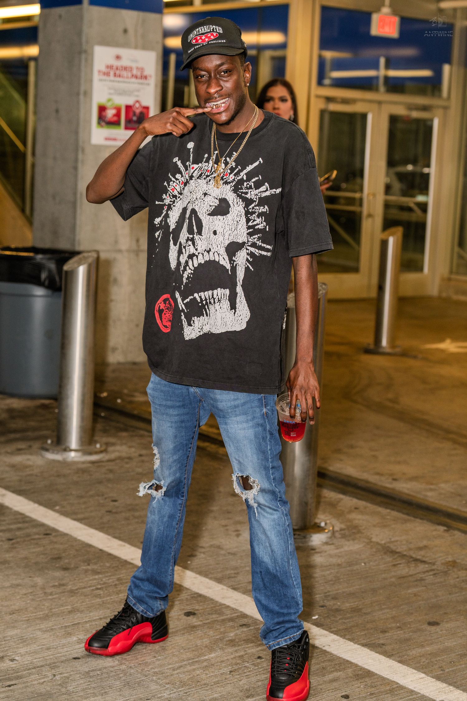 Young man in graphic skull tee, ripped jeans, and red black sneakers posing outdoors at night.