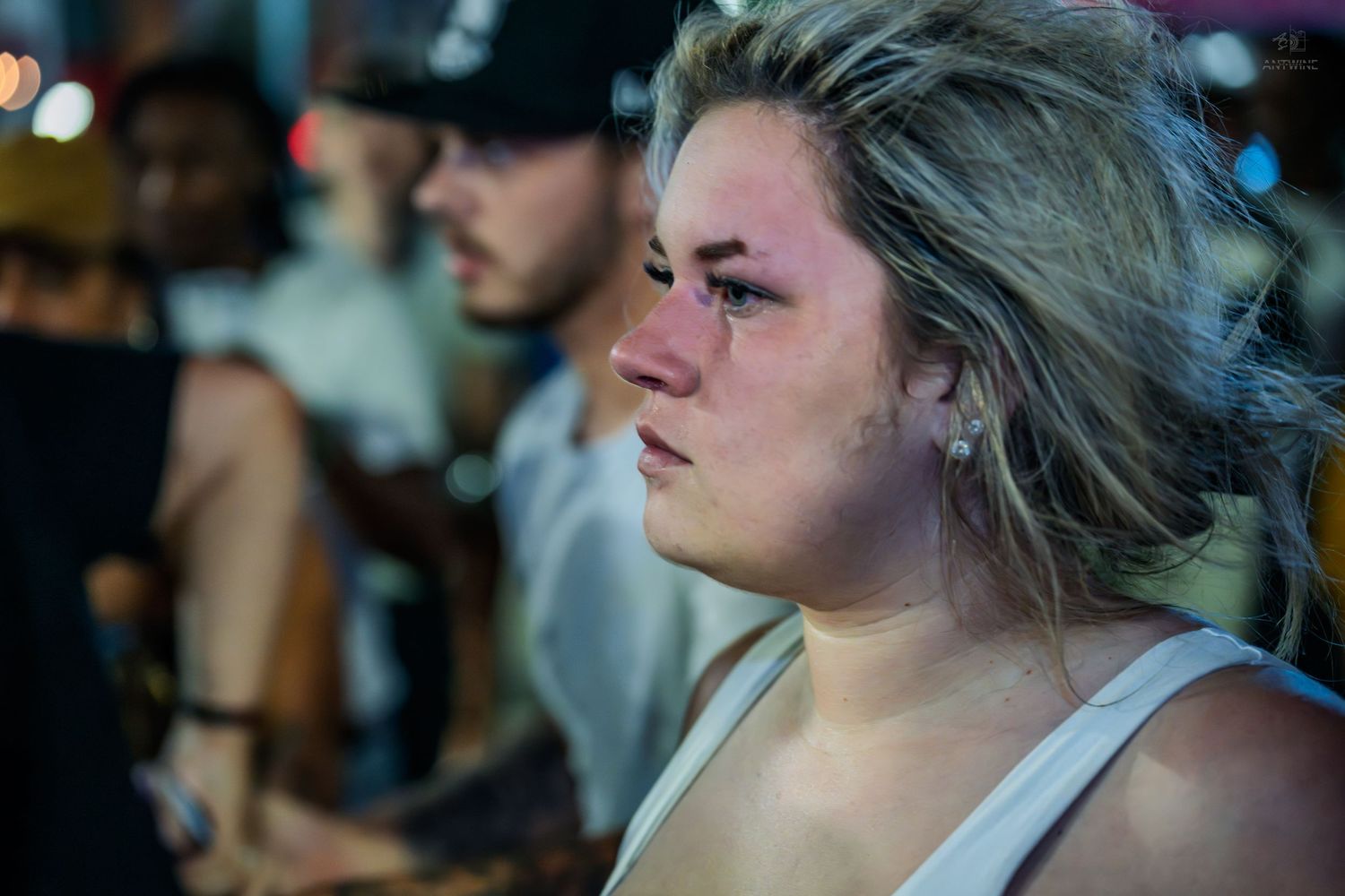 Emotional young blonde woman with a bruised eye looking distressed in a nighttime crowd.