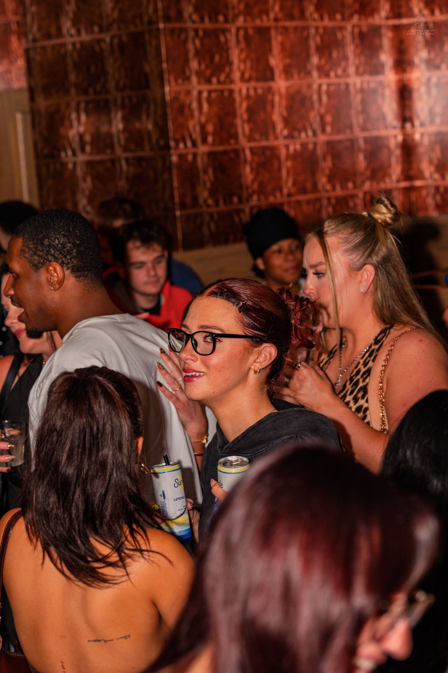 Woman in glasses whispering to friend at packed nightclub party night out.