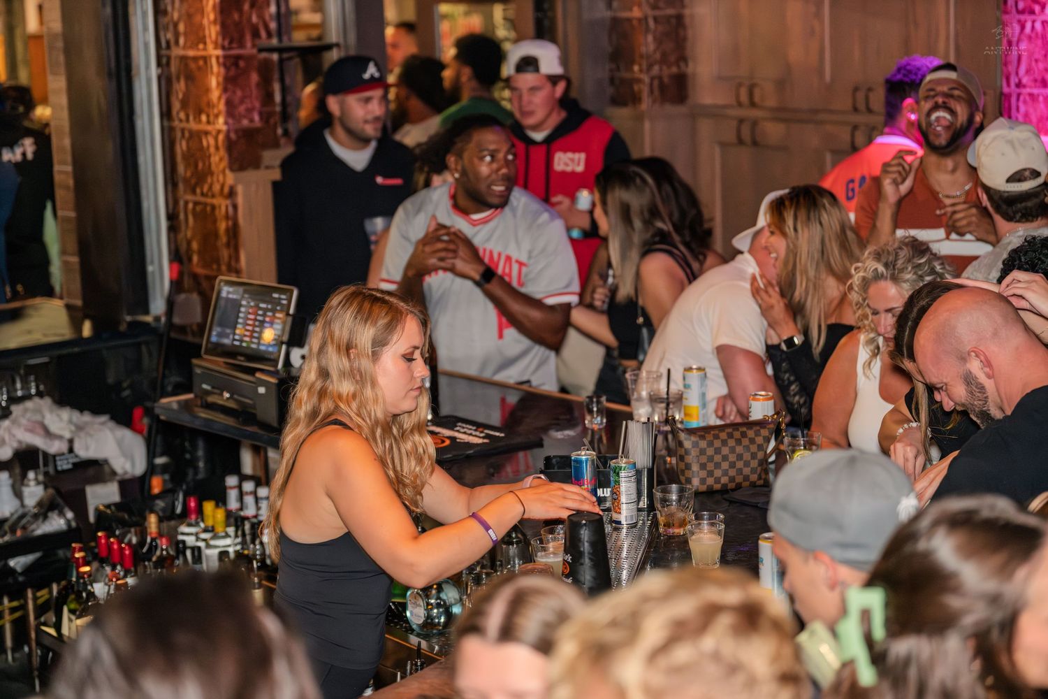 Busy bartender serving drinks to a large crowd at a vibrant nightclub bar.